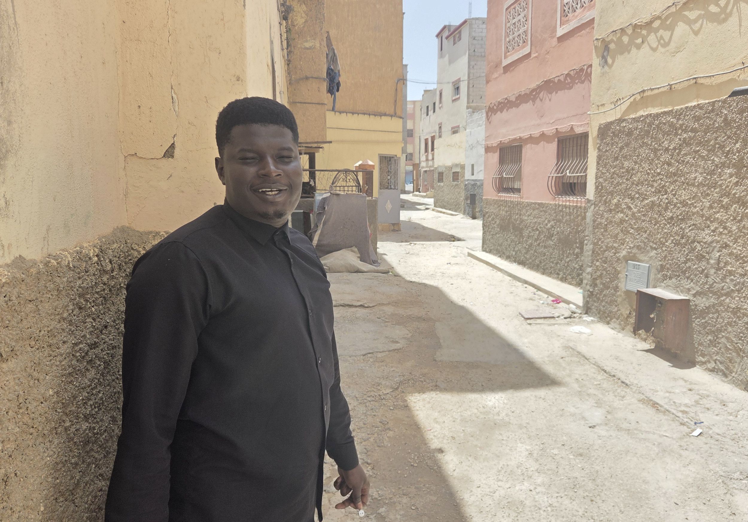 Man in zwarte kleding staat in een smalle straat tussen pastelgekleurde huizen.