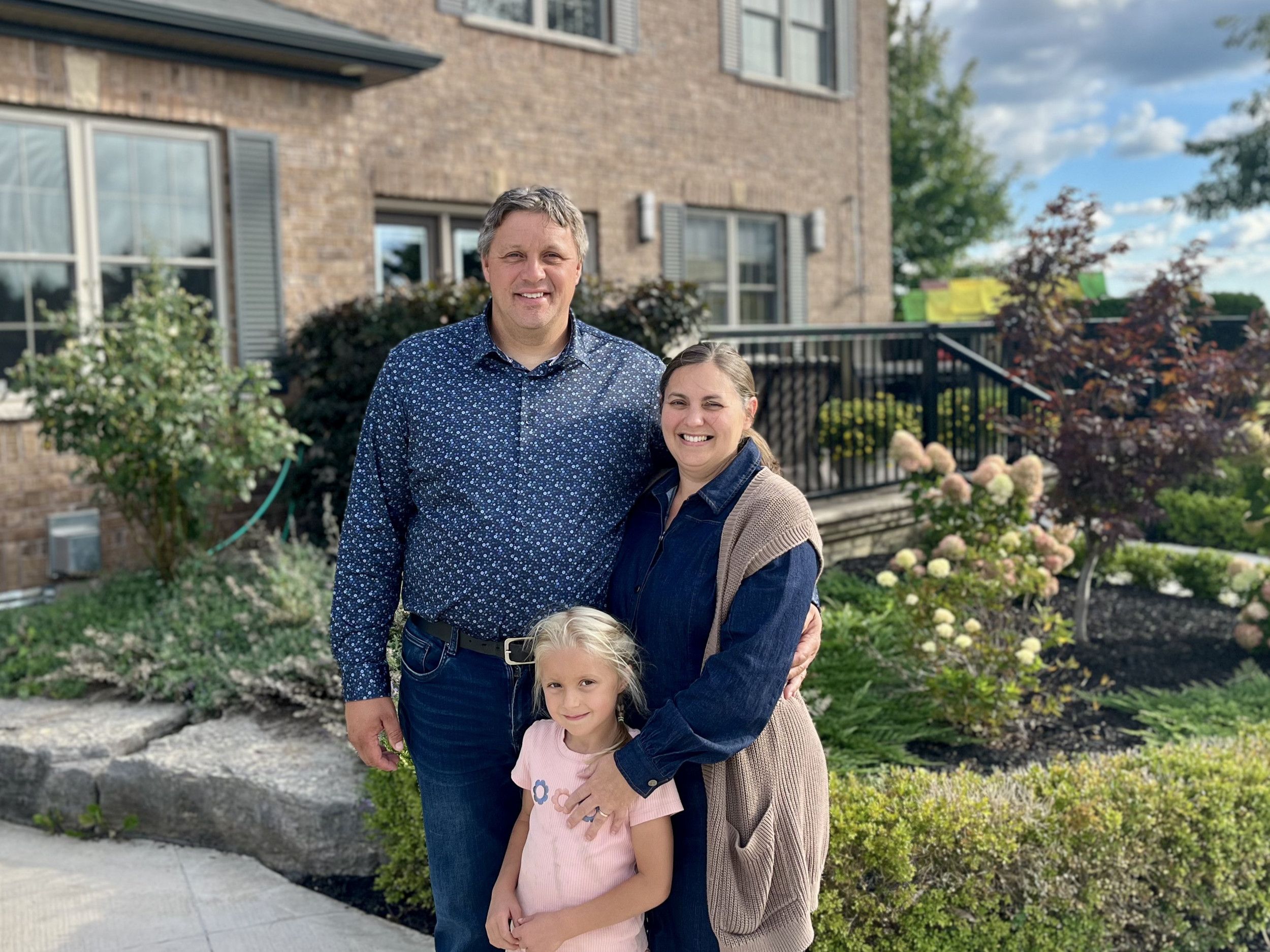 Vader, moeder en kleine dochter in de fraai vormgegeven tuin van een huis.