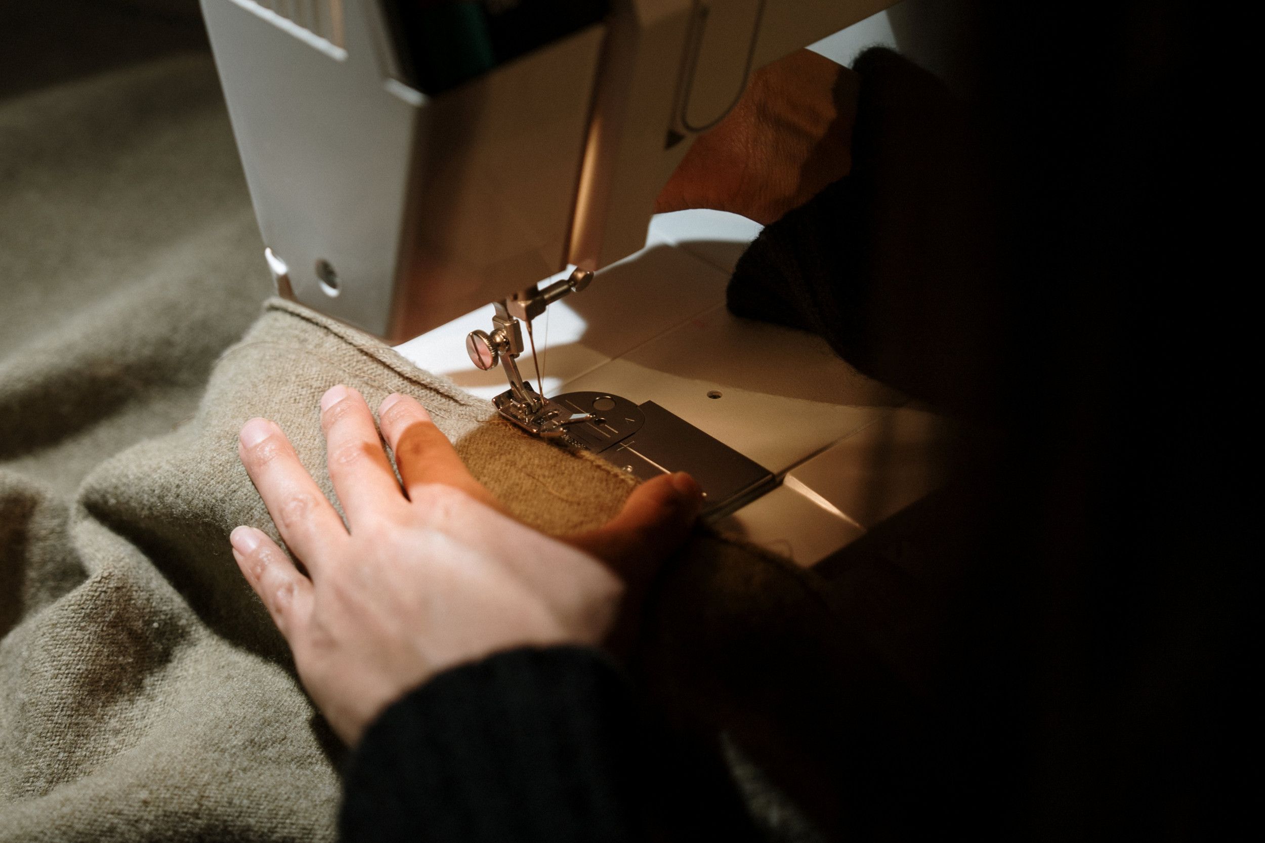 Iemand naait een lichtgroen kledingstuk. 