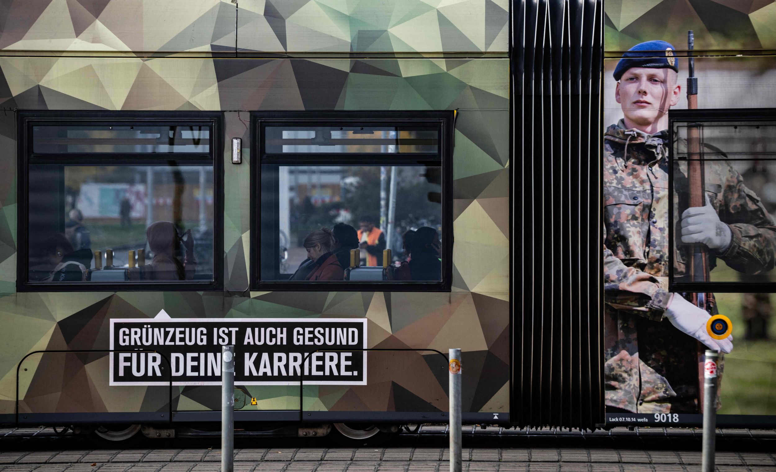 Afbeelding van soldaat op een tram, die in groen-bruine camouflagekleuren is gespoten.