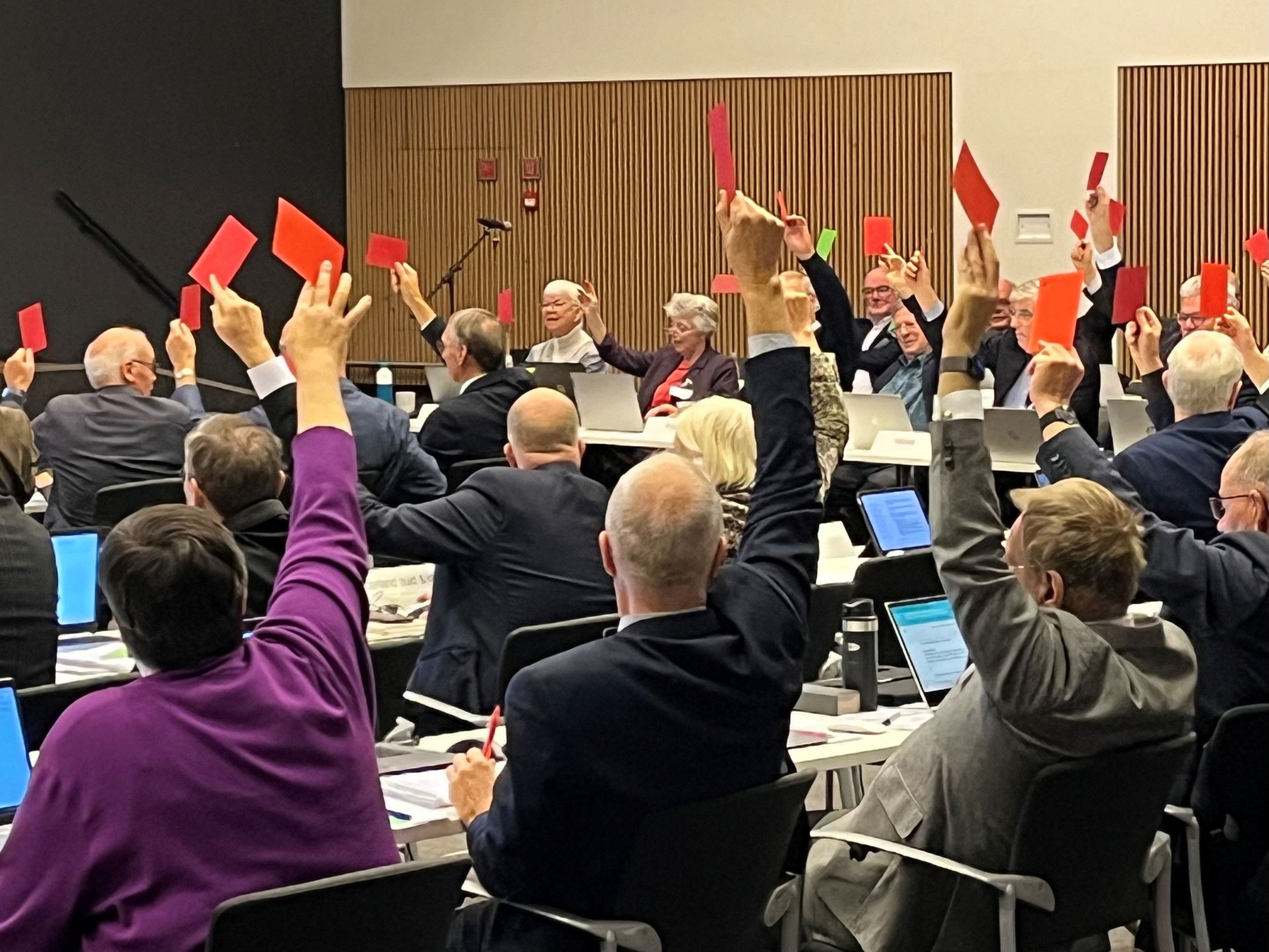 Een zaal vol mensen stemt door een rode of groen kaart in de lucht te steken.