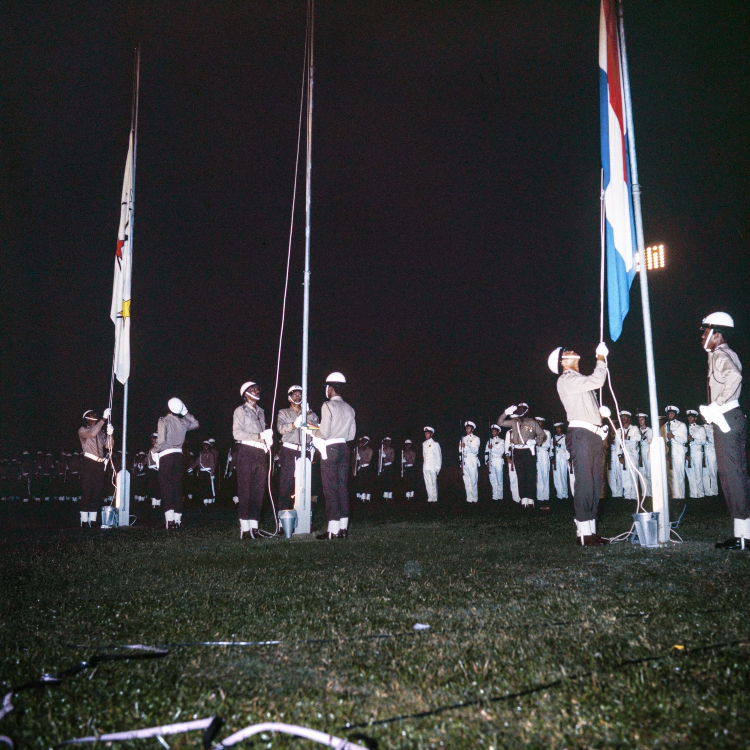 Mannen met witte helmen in de nacht, met touwen van de vlaggenmasten in hun handen.