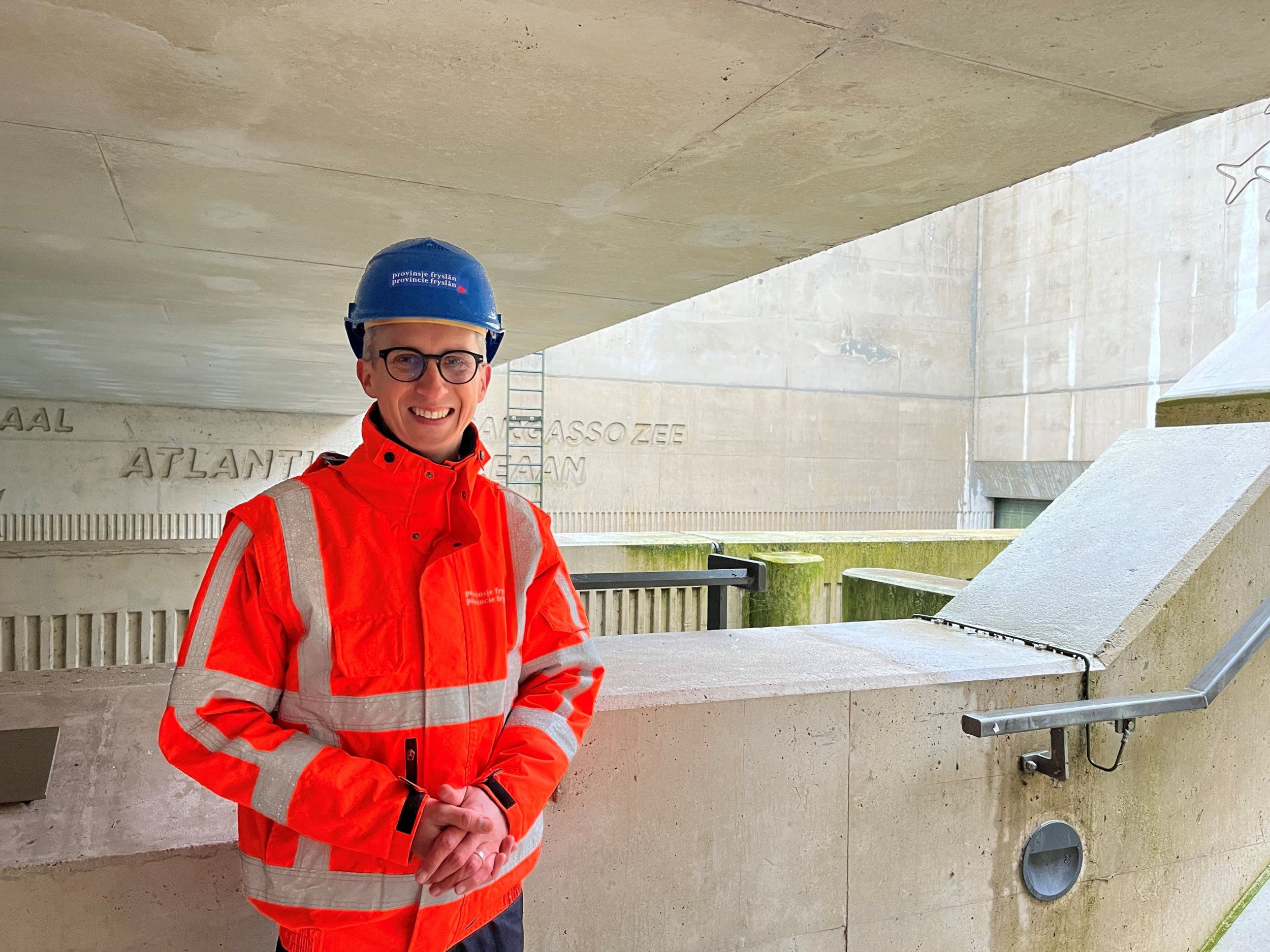 Man met blauwe veiligheidshelm op en met oranje hesje aan.