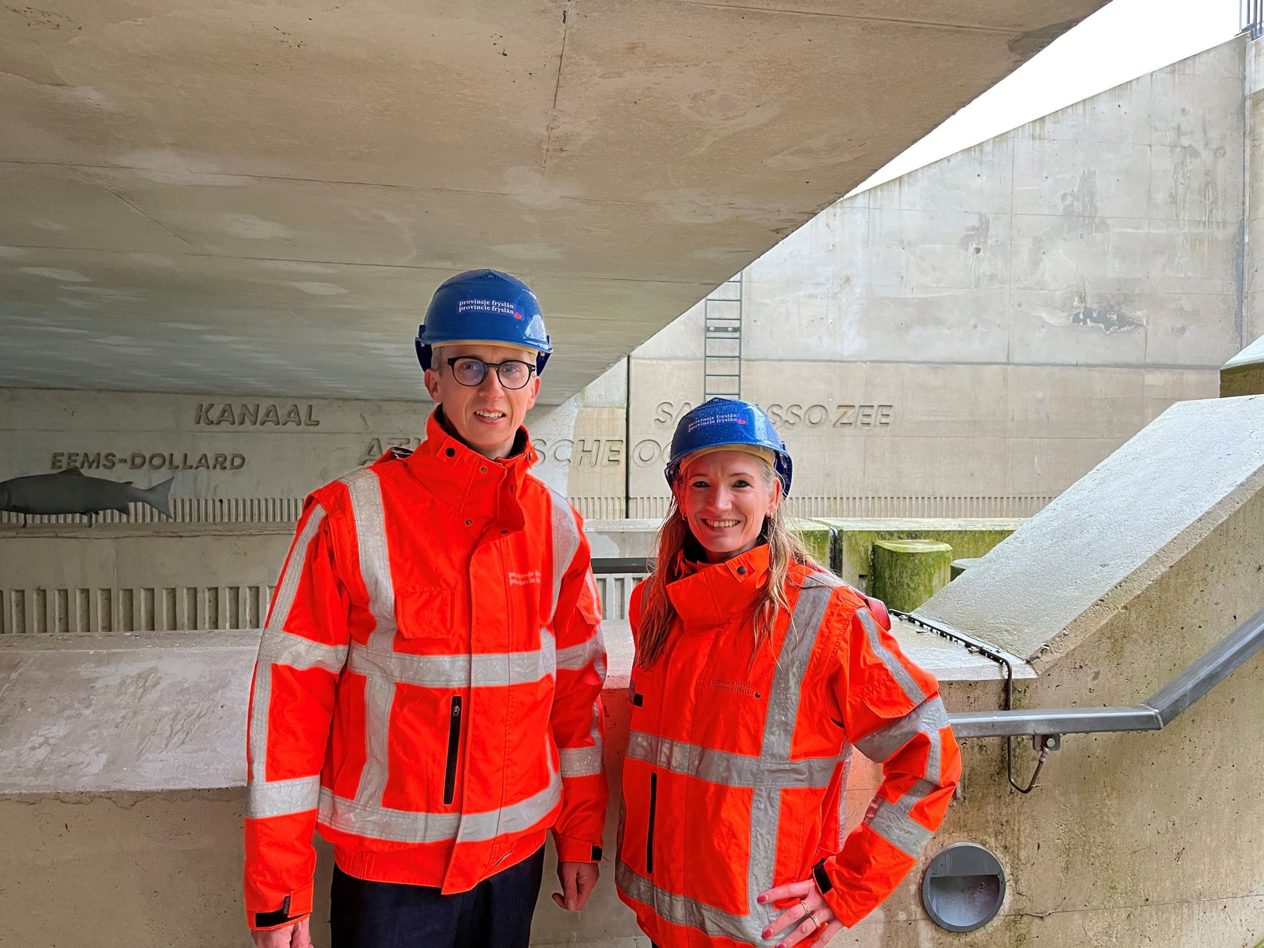 Een man en een vrouw met blauwe veiligheidshelm op en met een oranje veiligheidshesje aan.
