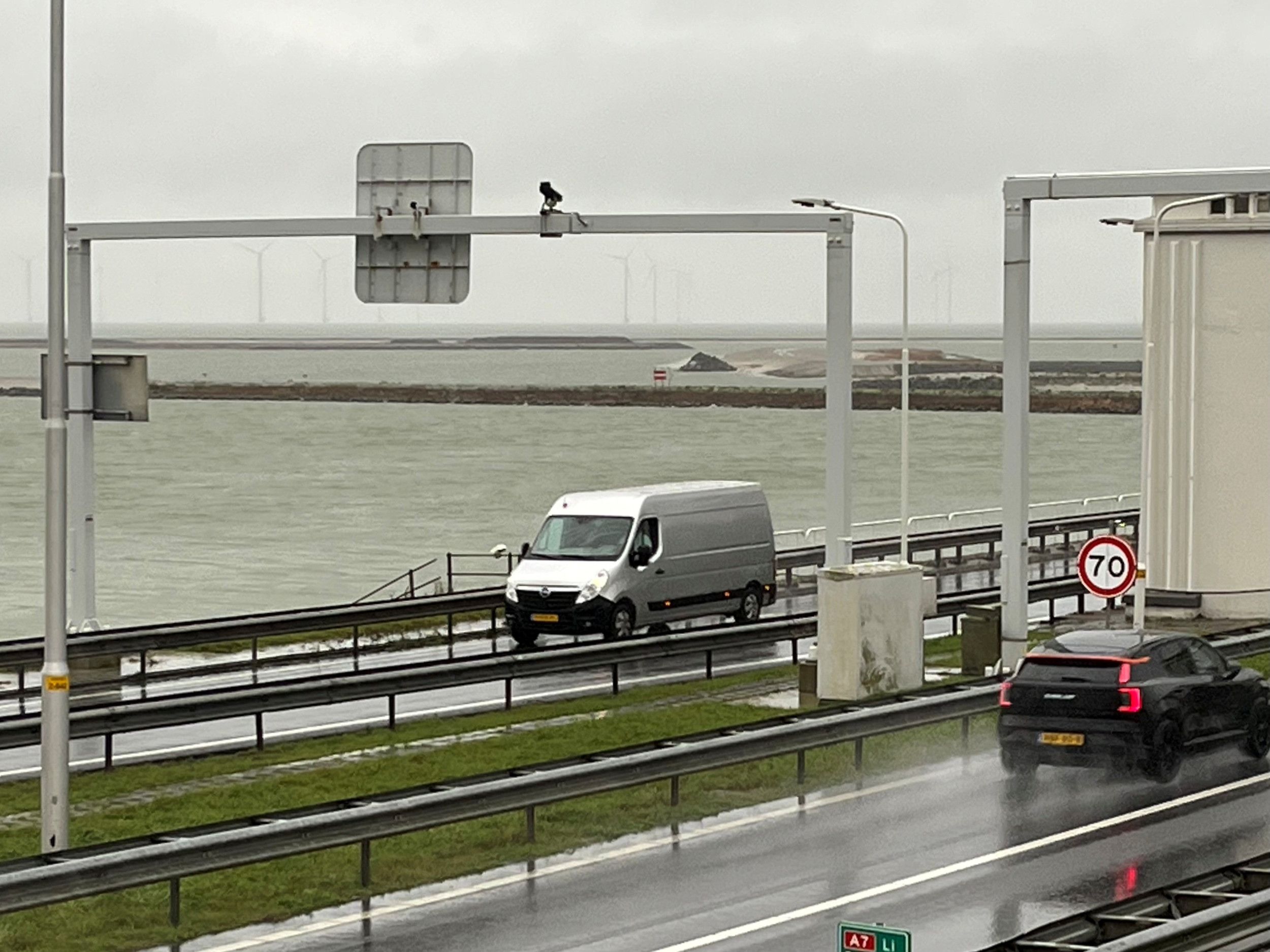 Snelweg met auto’s met op de achtergrond een windmolenpark en de contouren van dammen van steen.