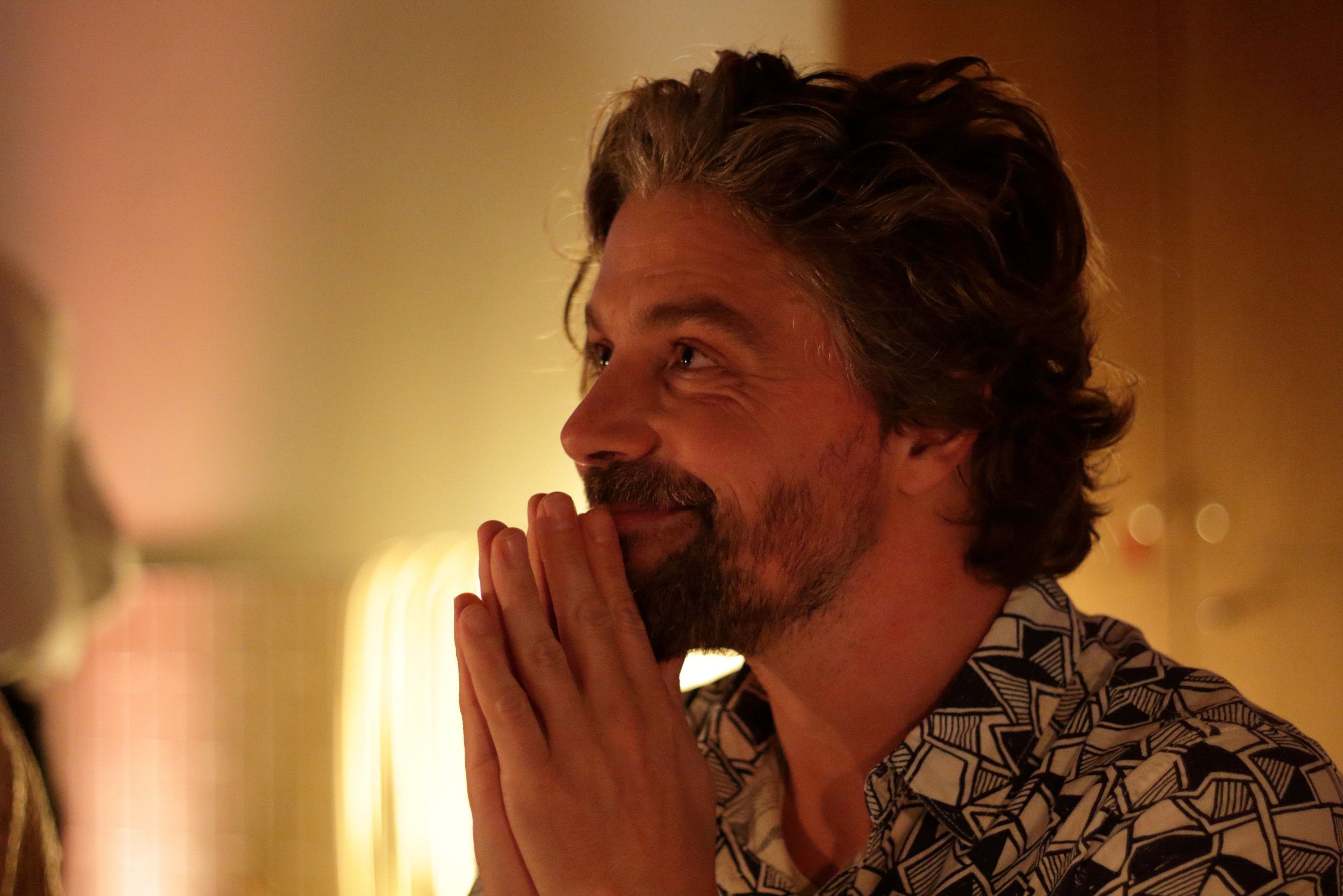 Portret en profil van een man met donker, halflang haar, een snor en een baard. Hij houdt zijn handen tegen zijn kin. 