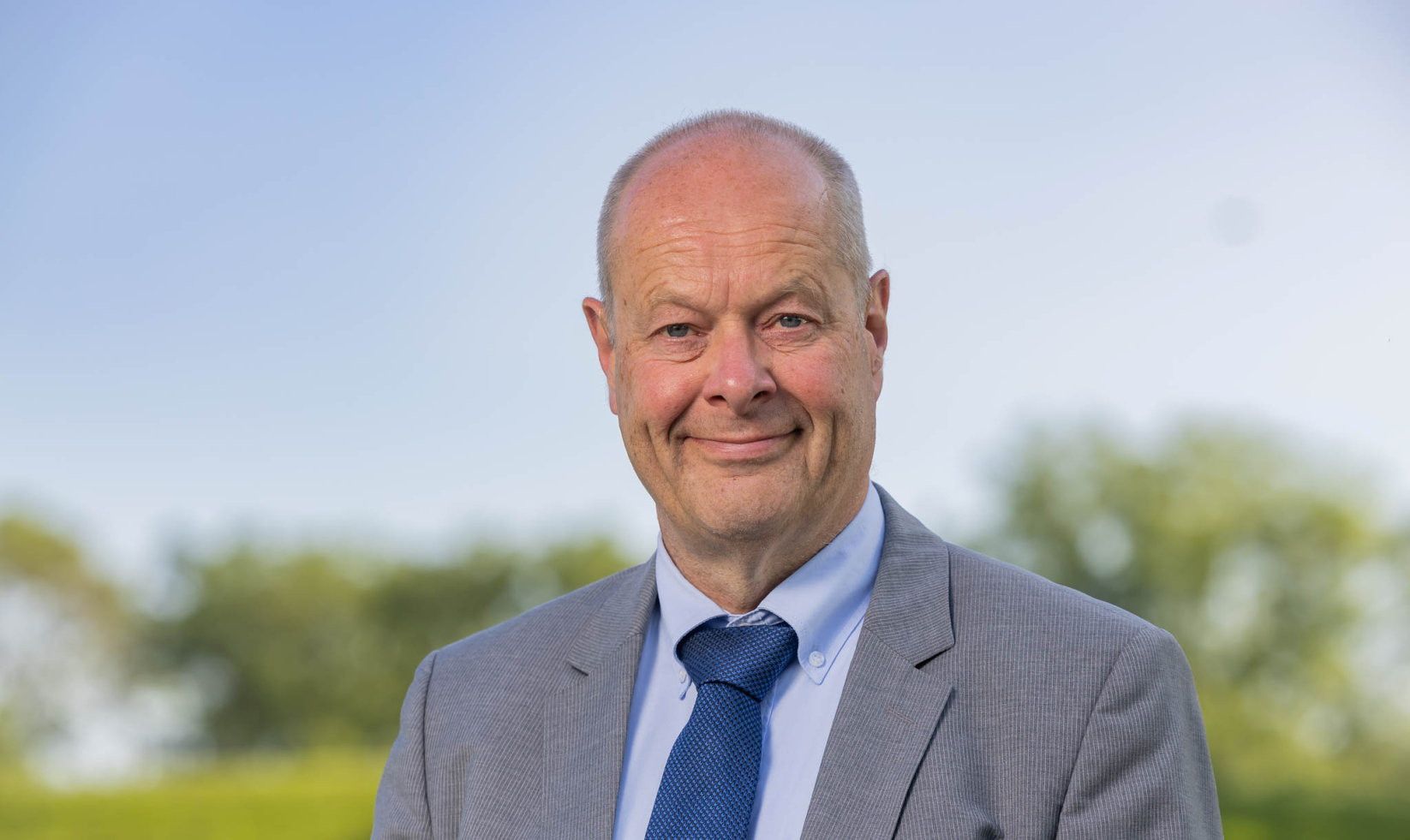 Kalende man met blauwe ogen, blauwe stropdas en grijs jasje. 