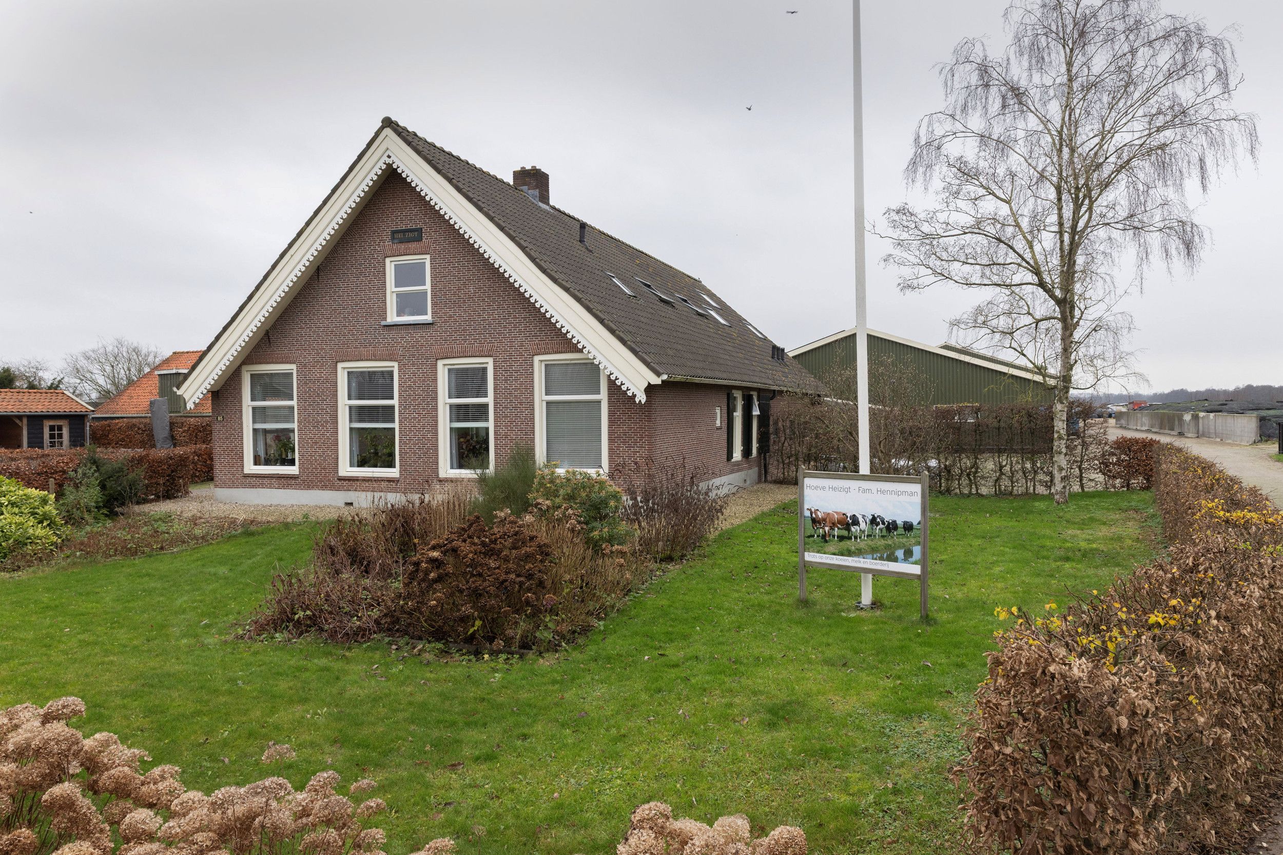 Woonhuis met stallen. In de tuin een bord met de tekst: Hoeve Heizigt, fam. Hennipman.