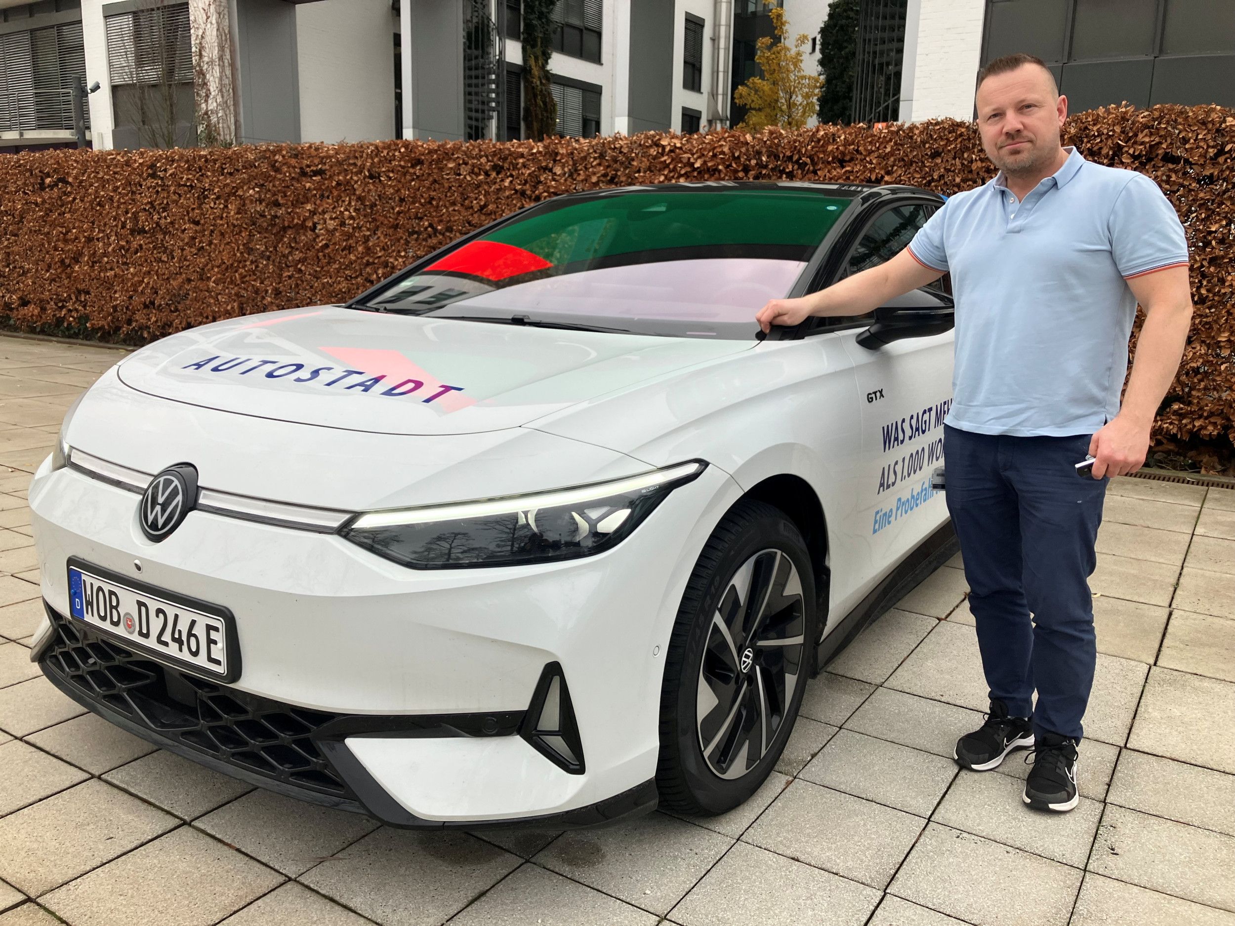 Een man poseert bij een witte auto. 