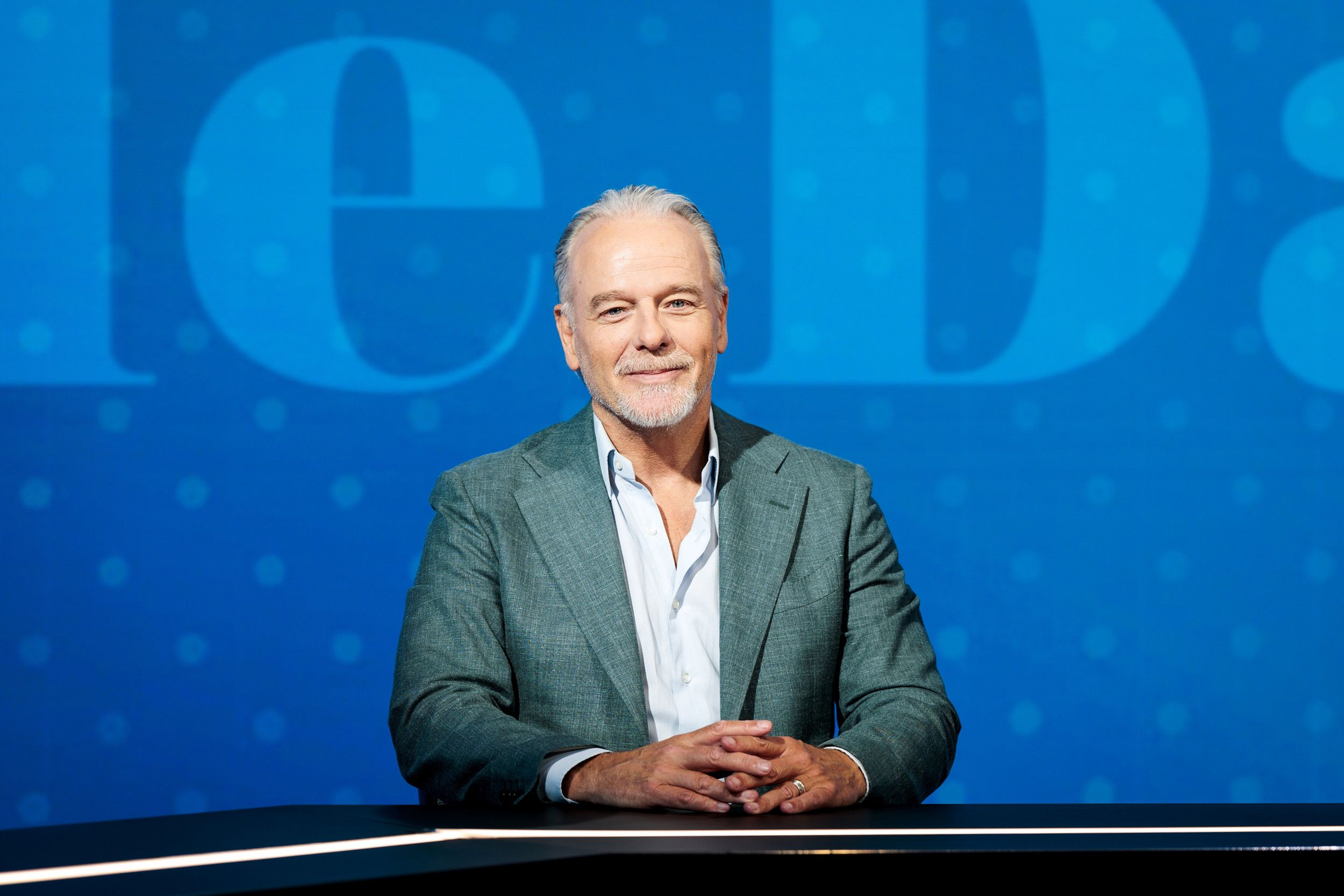 Man met grijze baard en groenblauw jasje. 