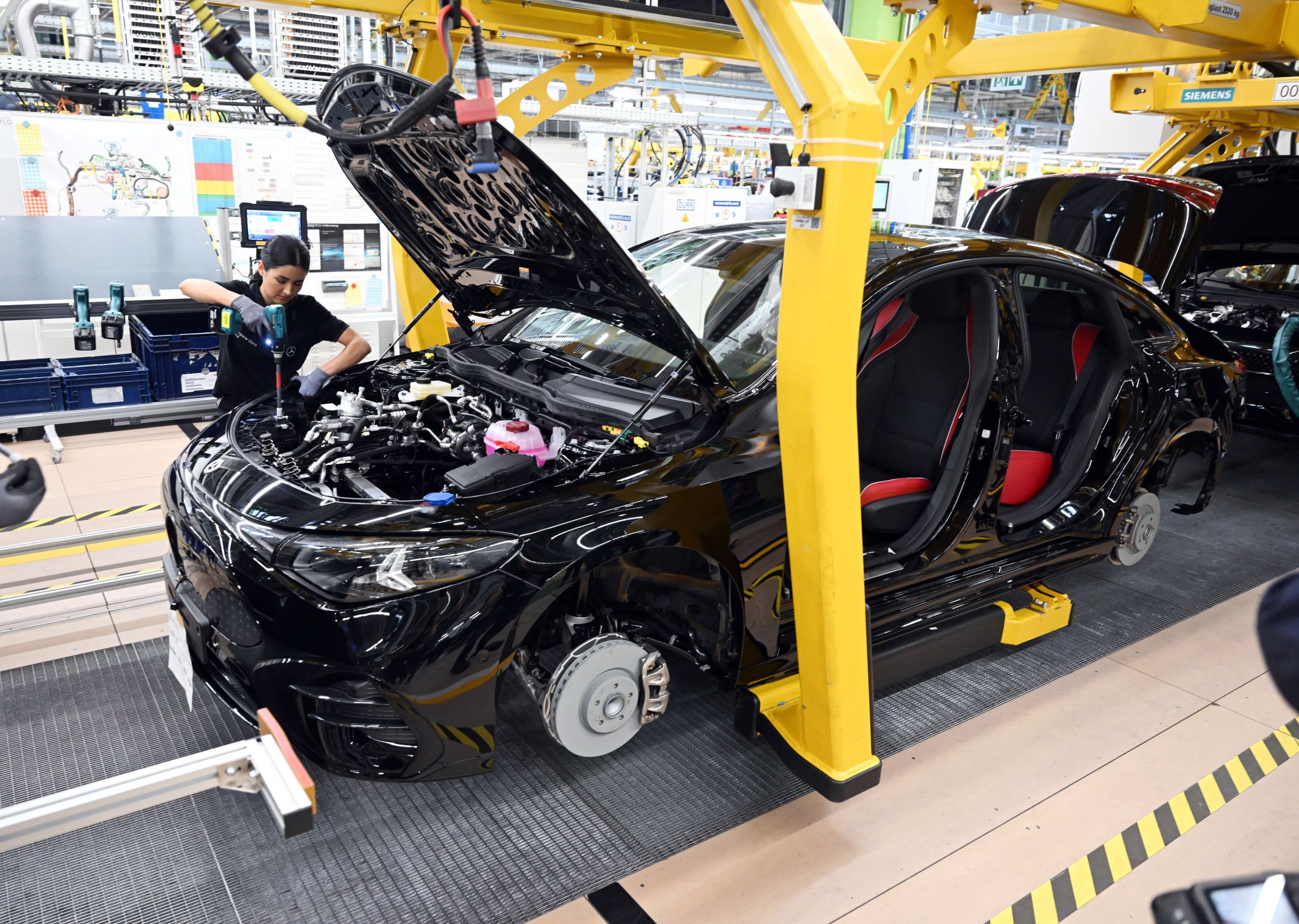 Een vrouw met een schroeftol werkt onder de motorkap van een zwarte Mercedes in een autofabriek in Duitsland. 