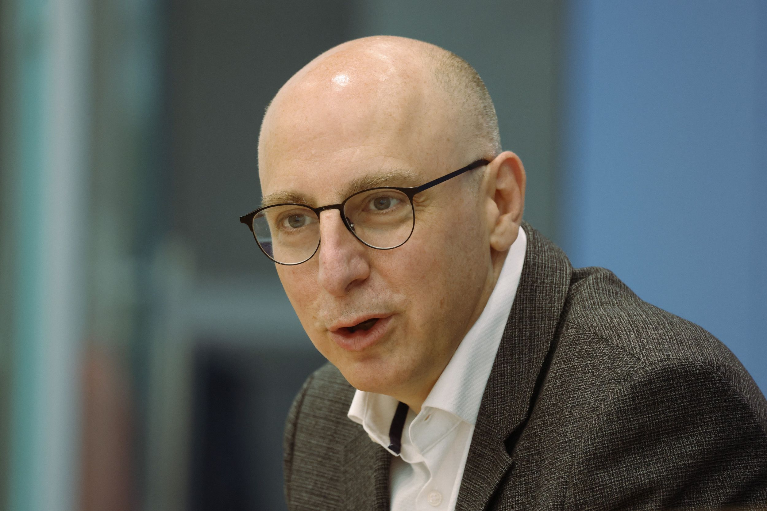 Een kale man met een bril op in pak. 