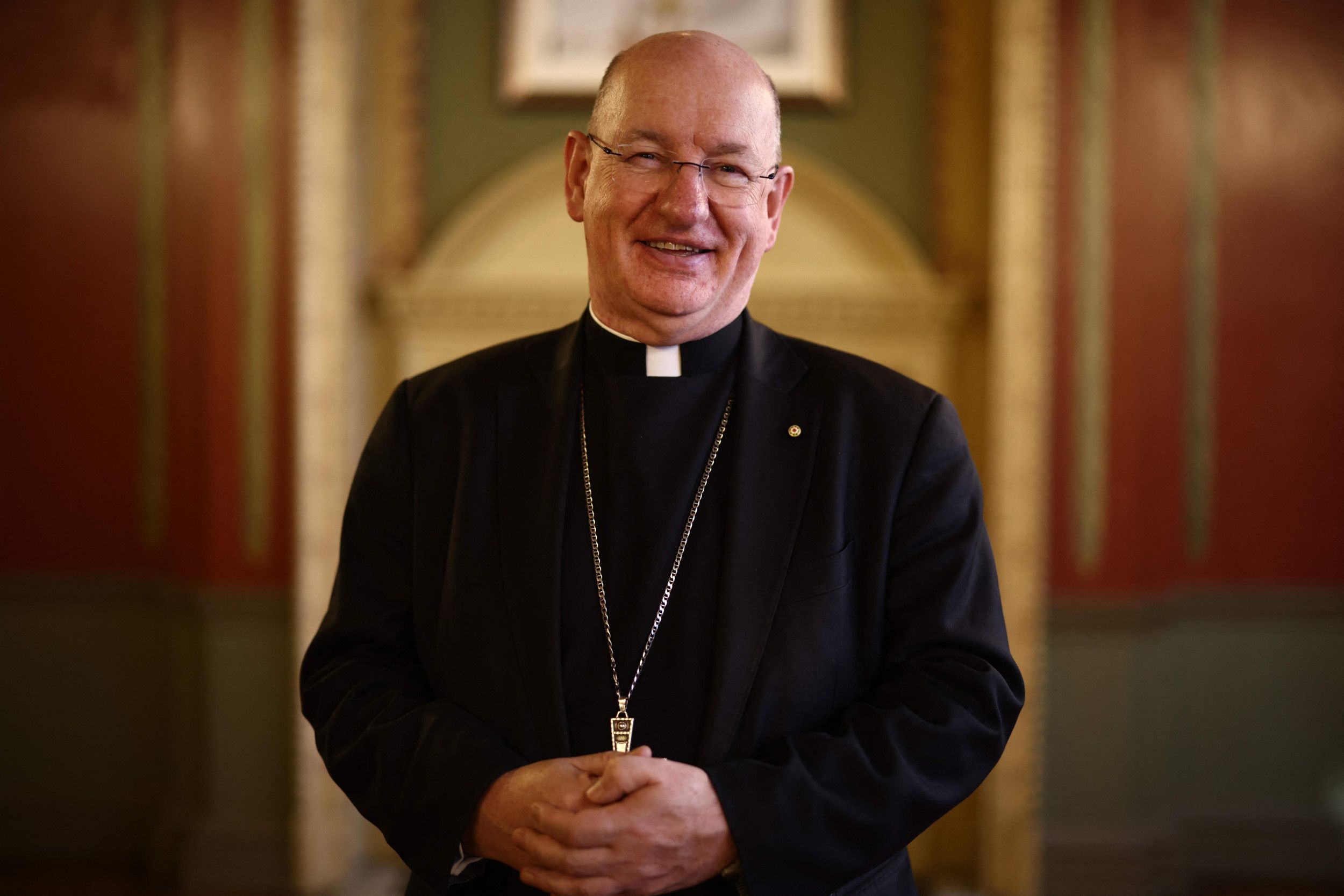 Richard Moth, een man met bril, gekleed in het zwart, een ketting om de hals.