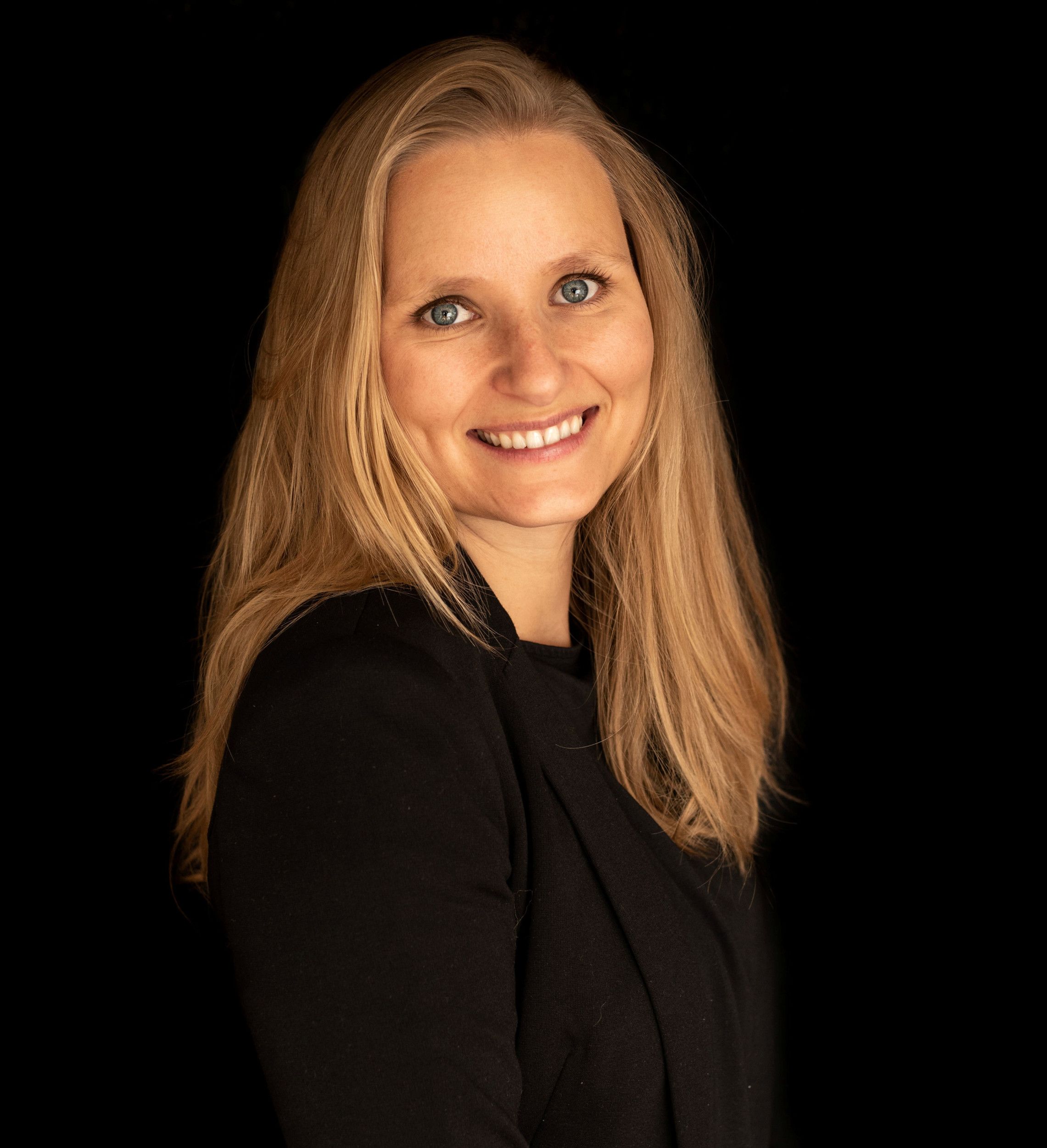 Vrouw met blond halflang haar, blauwe ogen en zwarte tuniek aan.