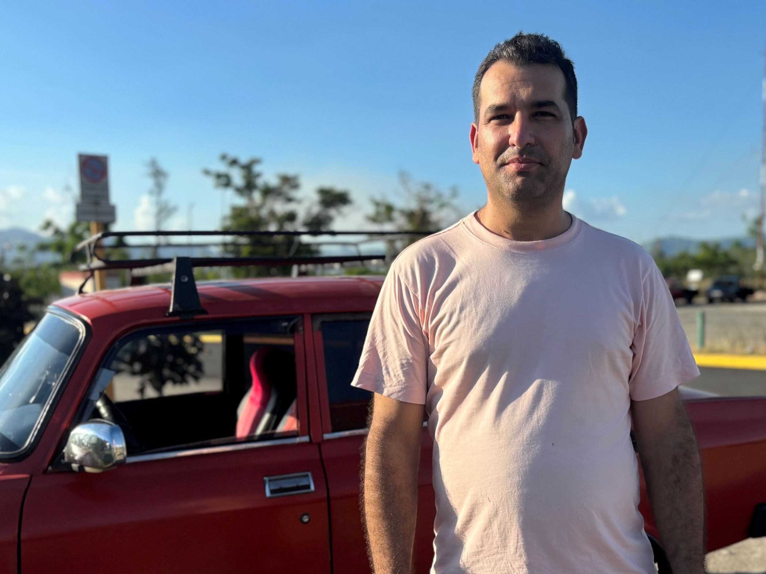 Man in T-shirt staat voor rode auto.
