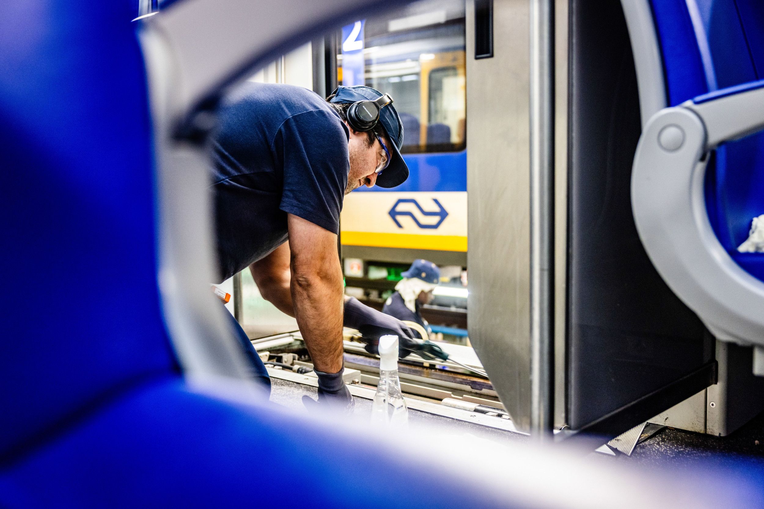 Een man met een koptelefoon op zit op zijn knieën en sleutelt in een trein.
