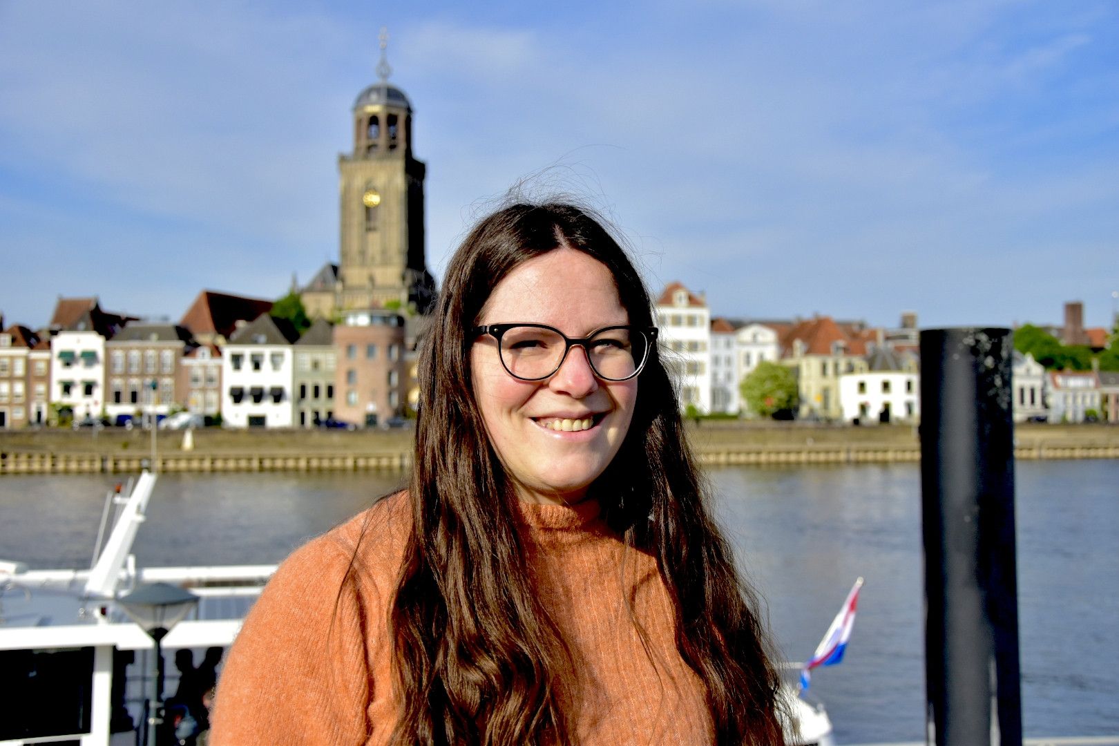 Lachende vrouw in oranje trui. Op de achtergrond een kerktoren.