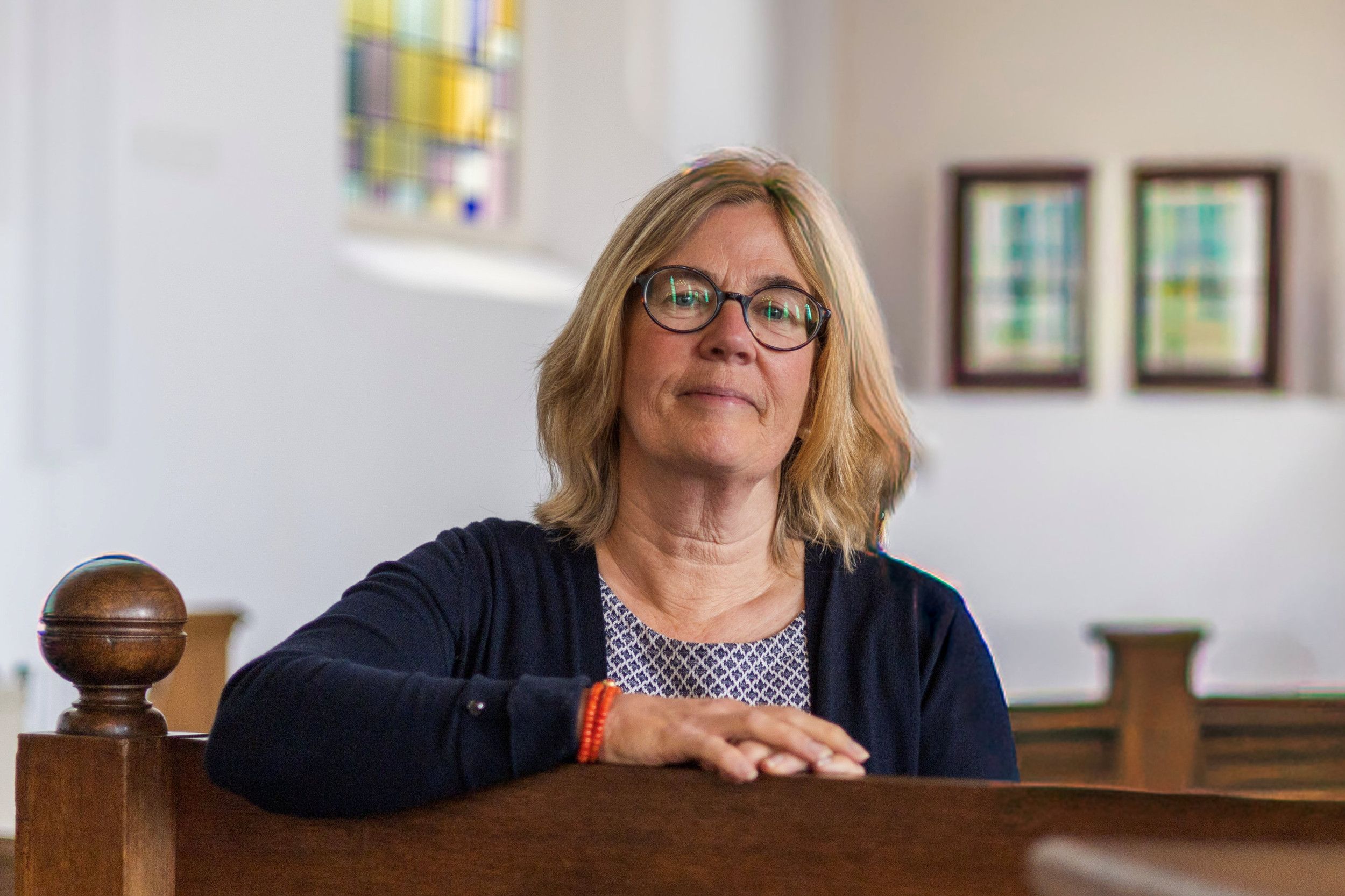 Vrouw met bril zit op een bank, met haar arm op de leuning.