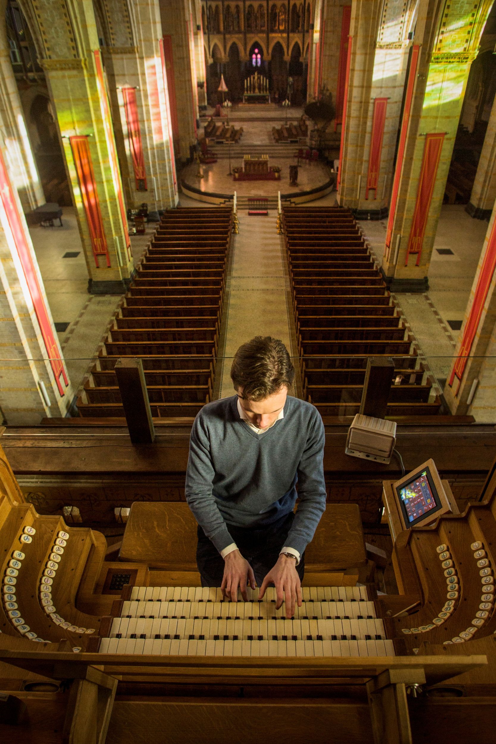 Een man speelt orgel in een grote kerk op een instrument met vier klavieren en tientallen registers.