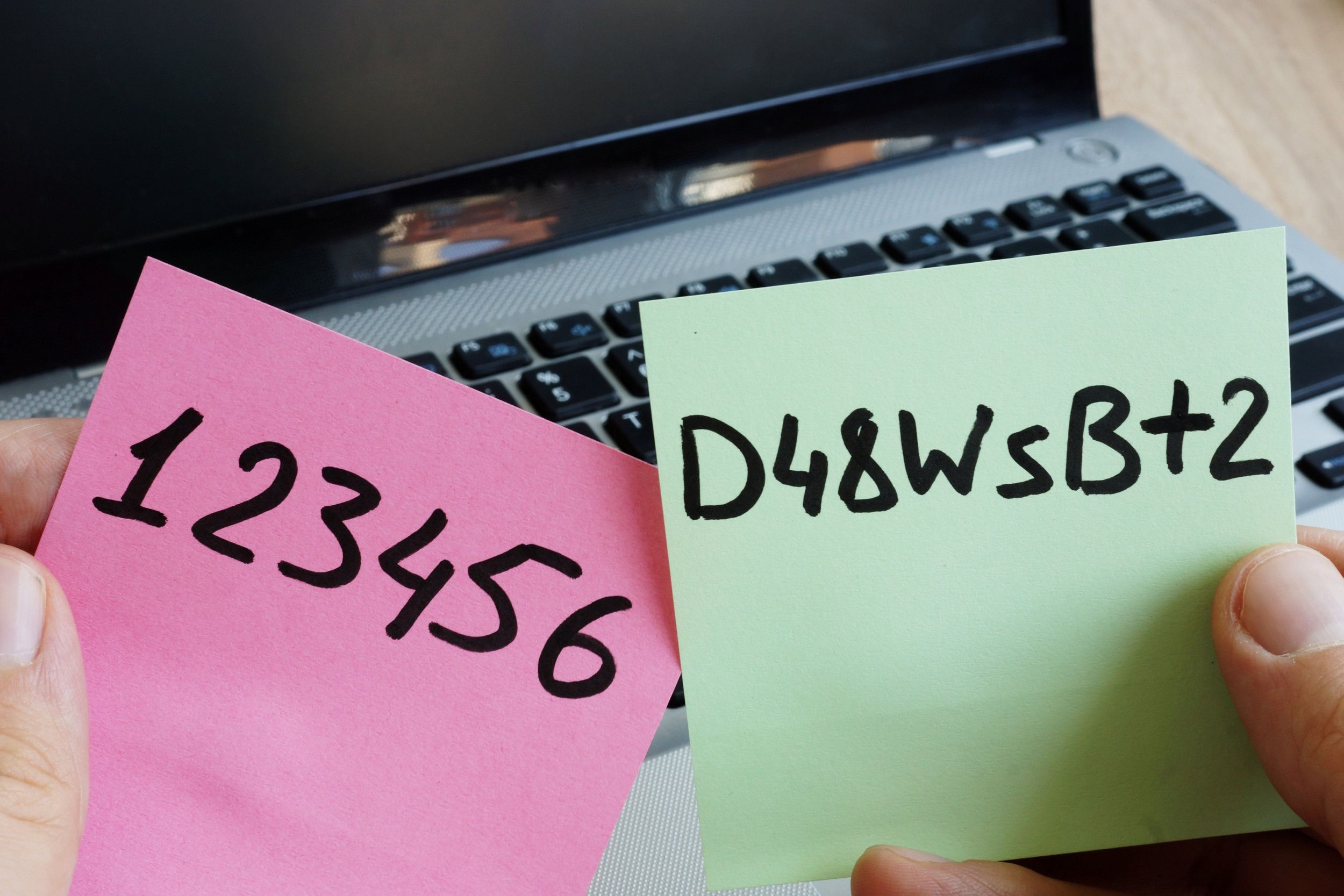 Zwarte letters en cijfers op een roze en groen briefje, met op de achtergrond een laptop.