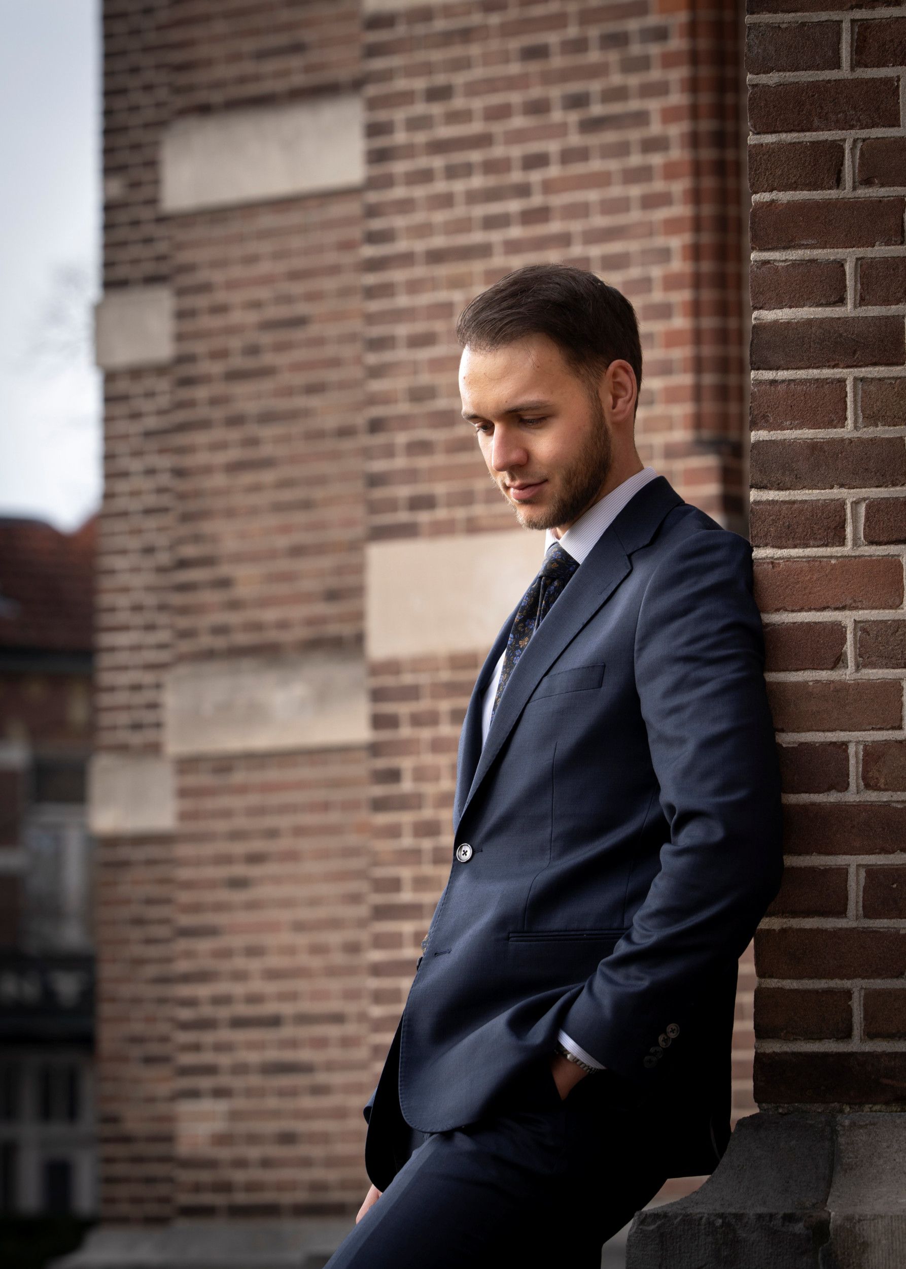 Jongeman met baardje, gekleed in een pak met stropdas, staat tegen de steunbeer van een oude kerk.