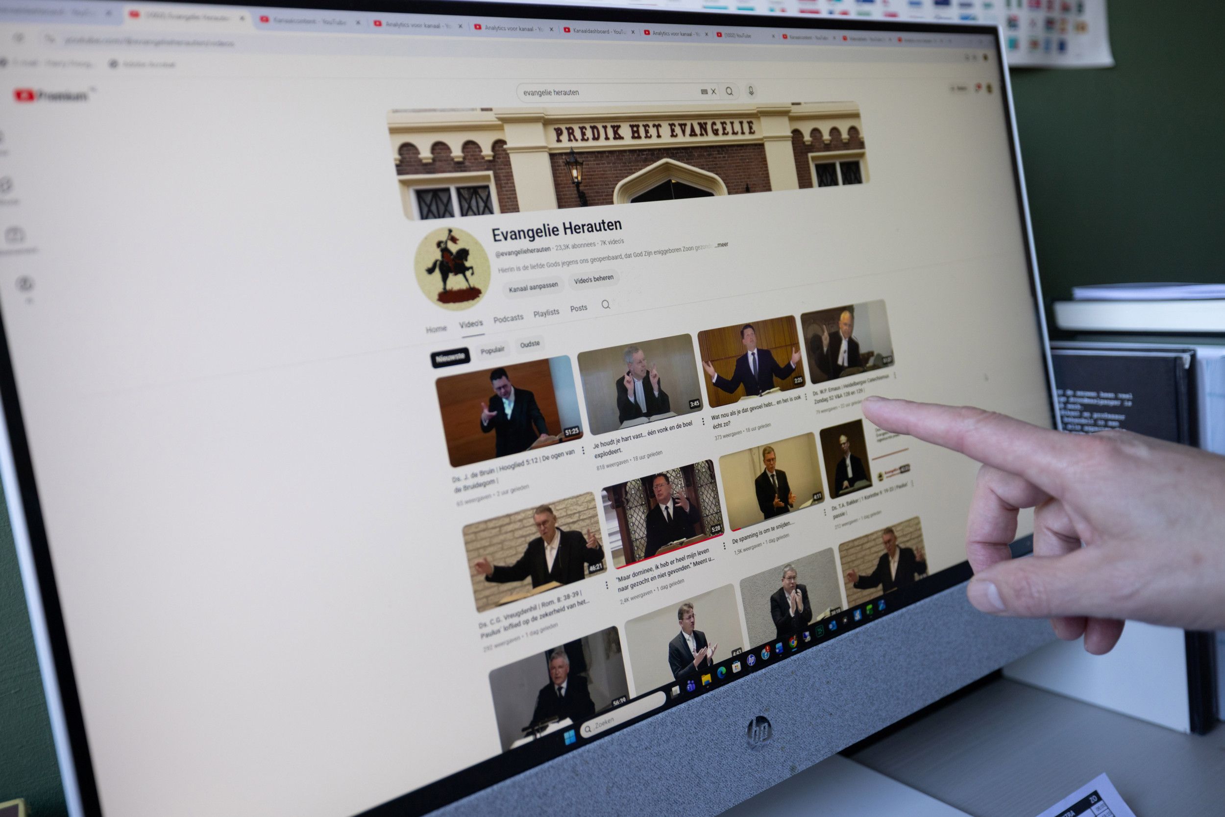 Een YouTubepagina met preekvideo’s staat open op een computerscherm. Een vinger wijst ernaar.