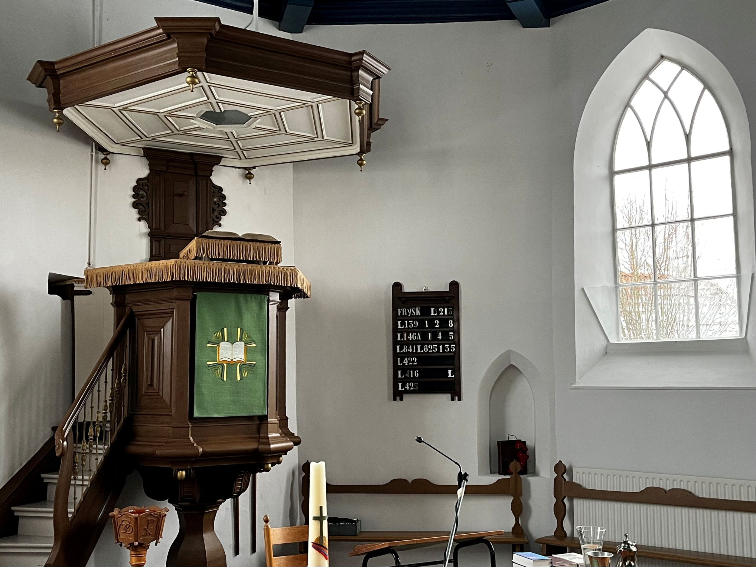 Donkere houten preekstoel, psalmbord en hoog raam. 