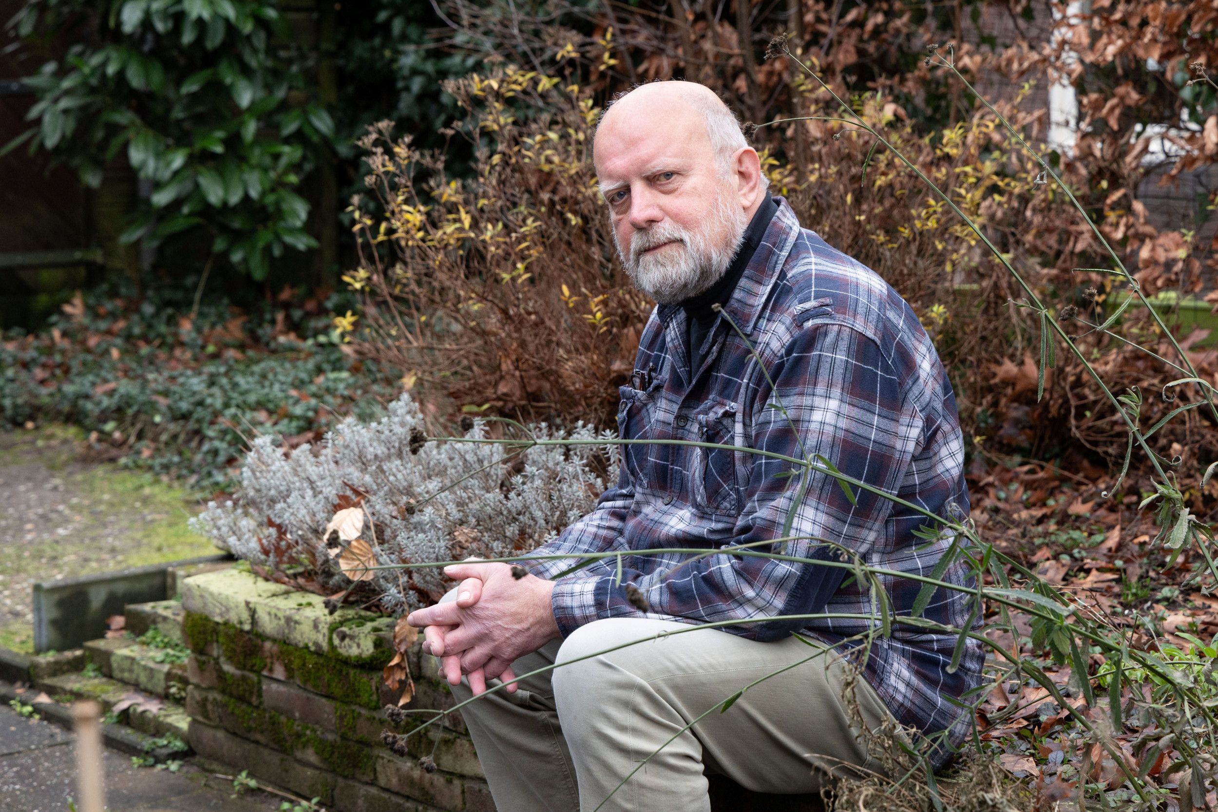 Kees Bevaart, een man met grijs haar, baard en ruitoverhemd, zittend in een tuin.