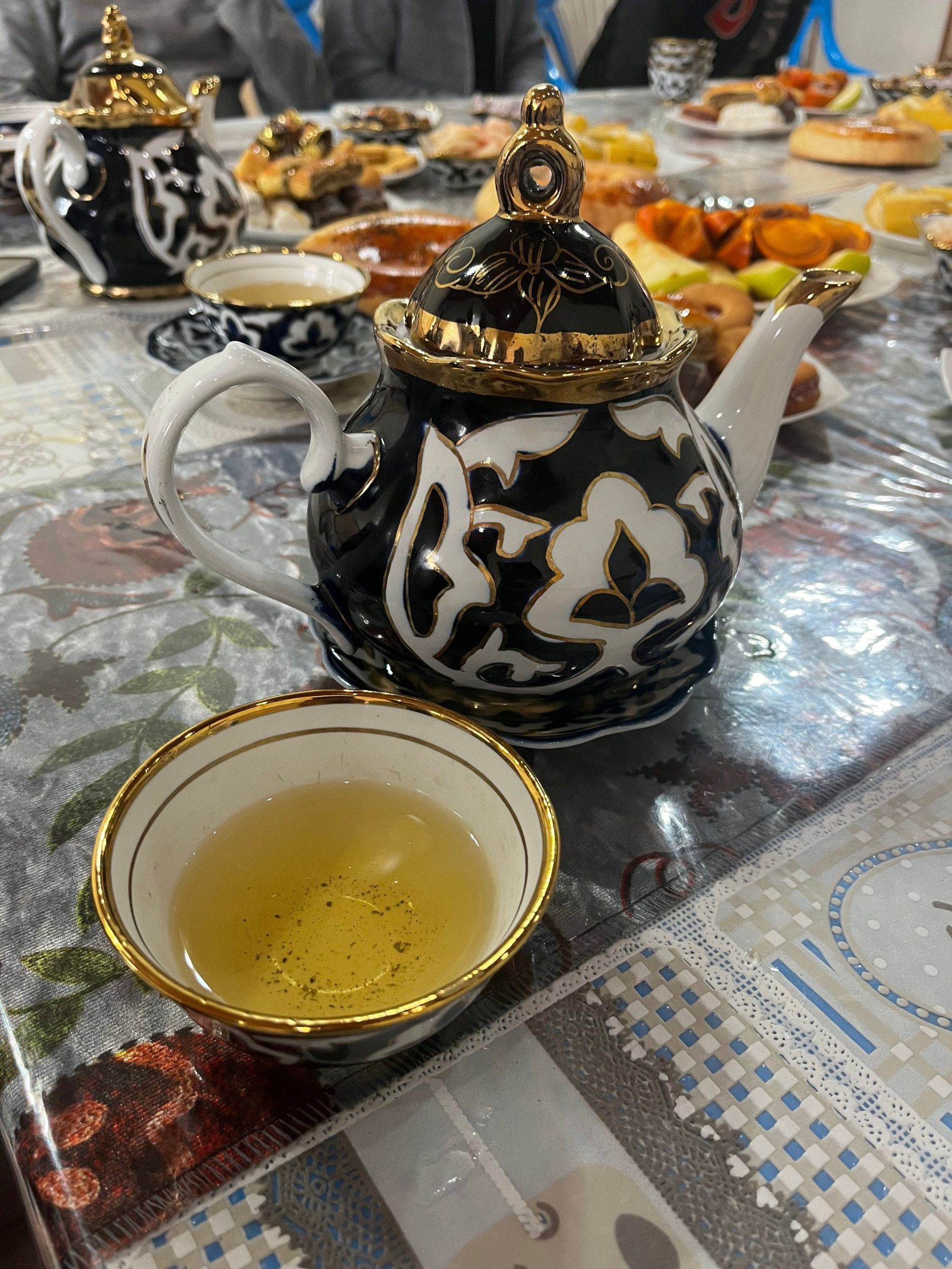 Een met thee gevuld wit schaaltje met gouden randen staat naast een zwart-wit-goud versierde theepot.