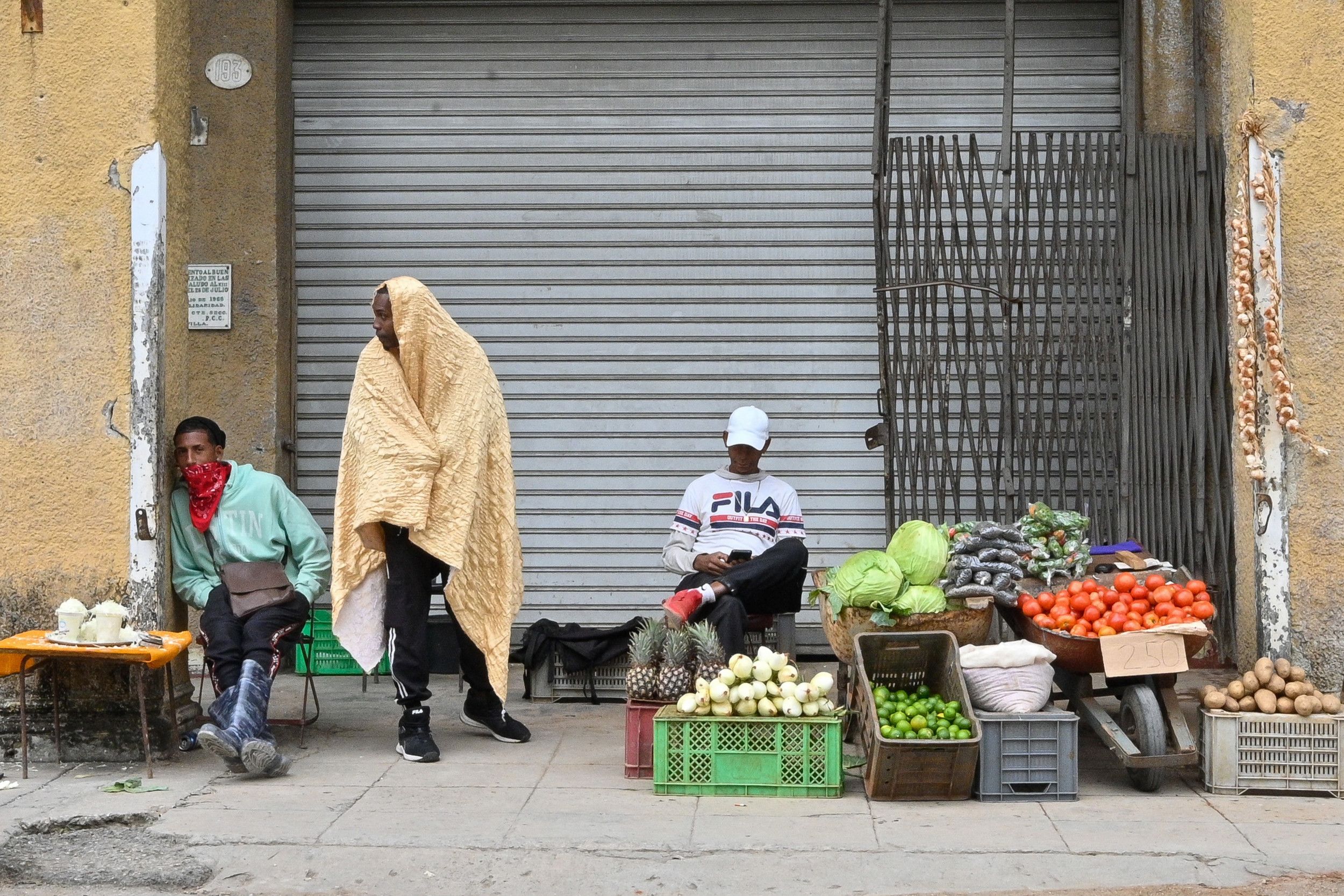 Drie mannen stallen langs de weg in een paar kratten en dozen groente en fruit uit.