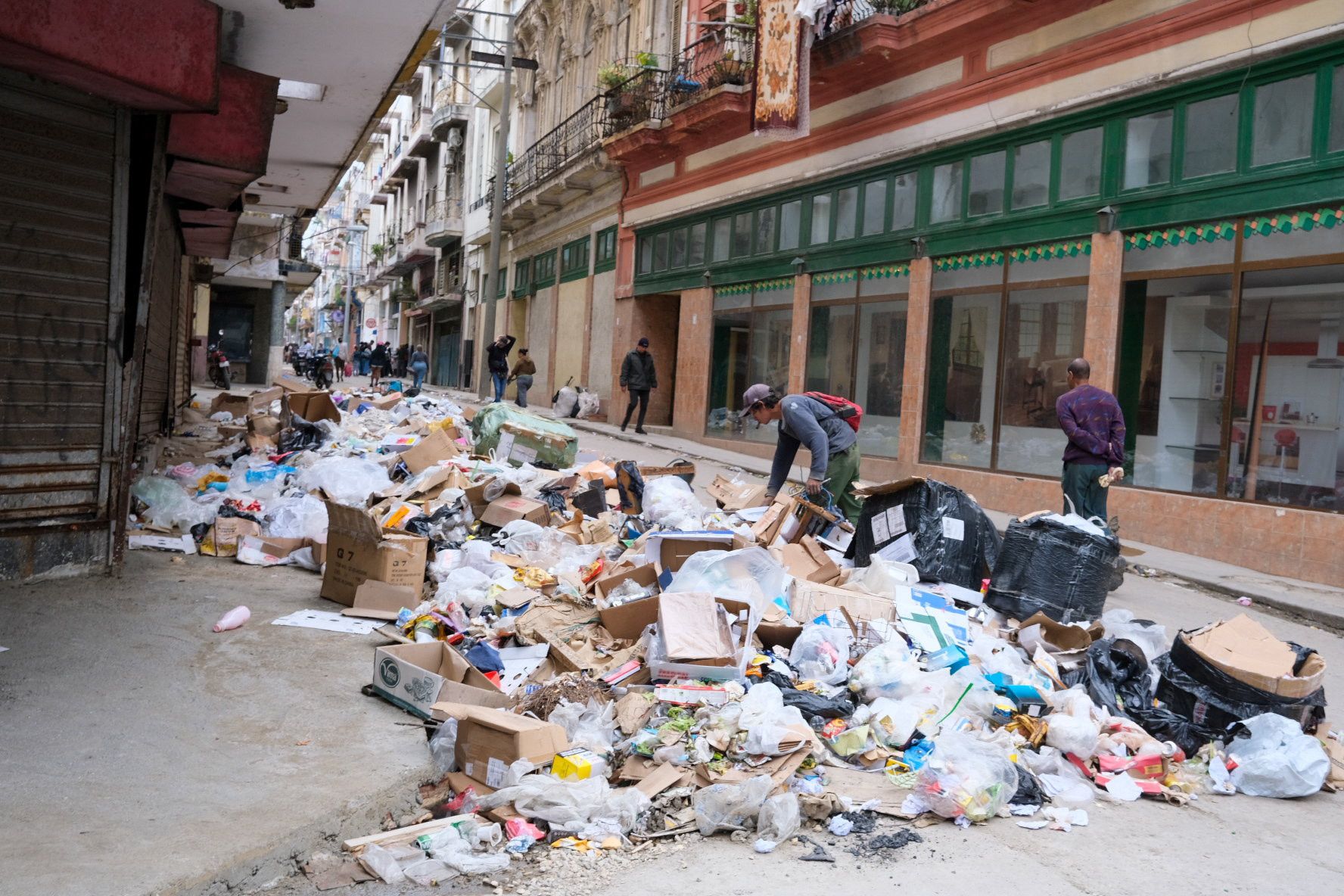 Man met een petje staat gebukt over een berg vuil en karton dat midden op de straat ligt.