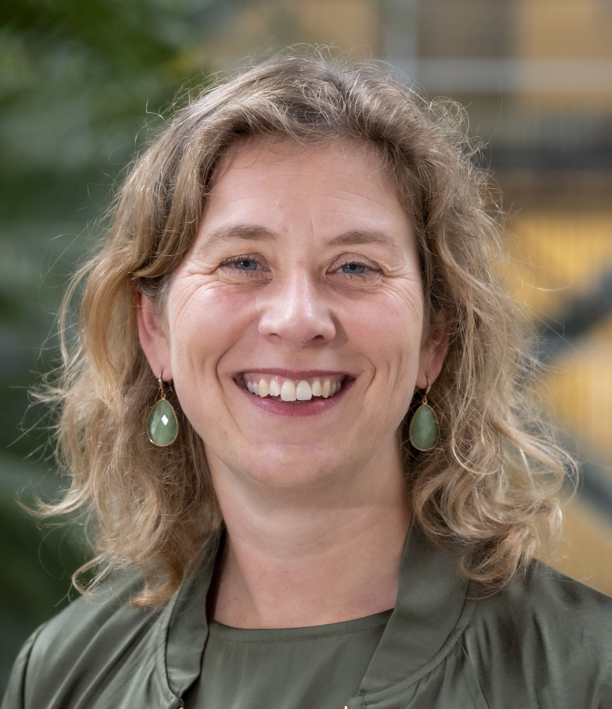 Vrouw met blonde krullen en groene jurk en dito oorbellen. 