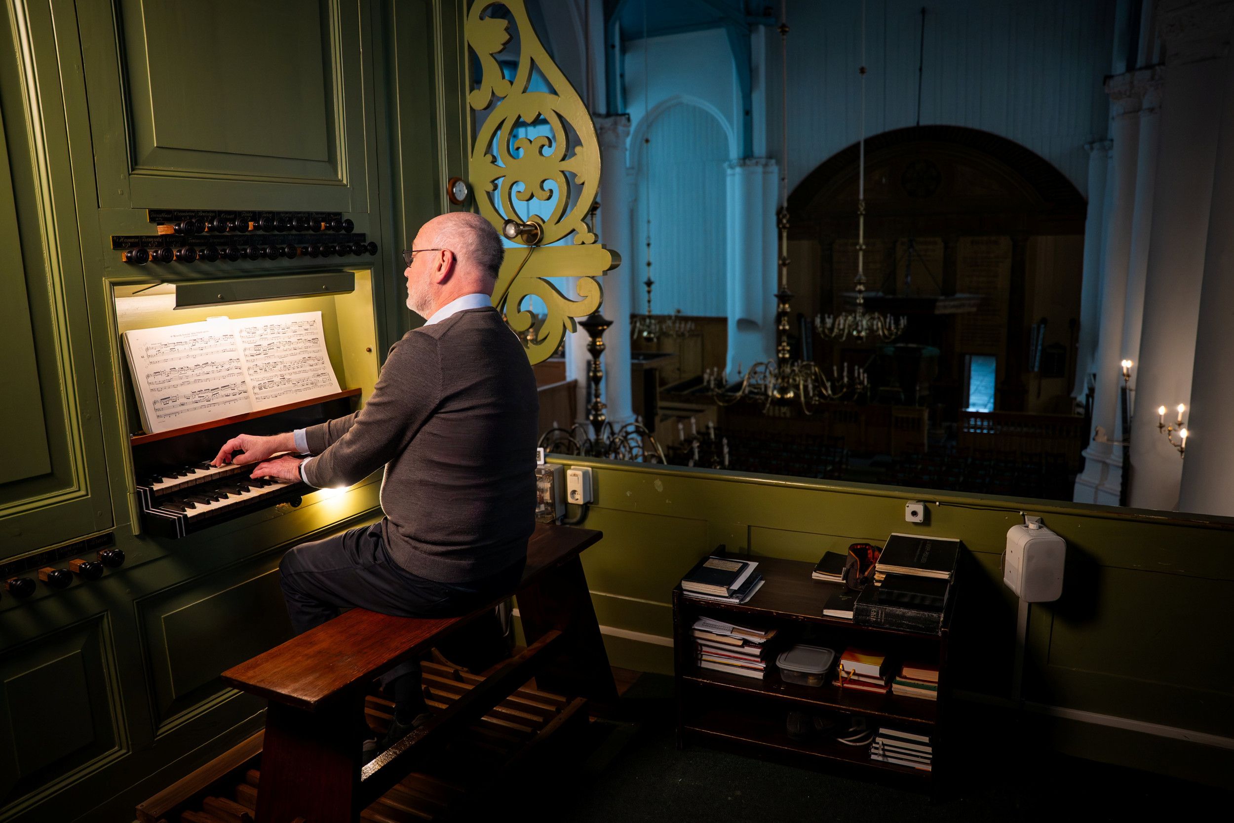 Een man bespeelt het orgel in een oud kerkgebouw. In de kerk hangen kroonluchters.