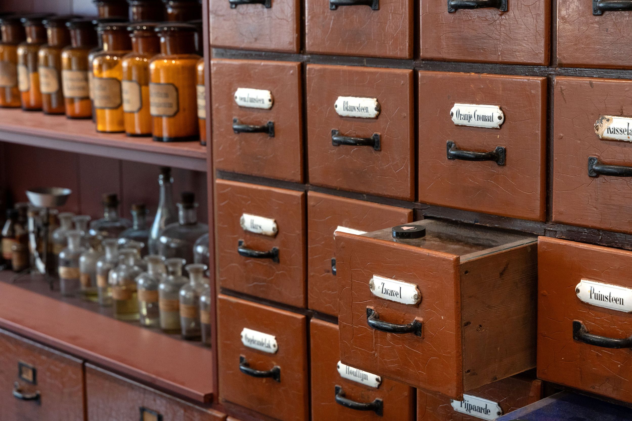 Er staat een lade open in een kast. Op de achtergrond zijn wat planken te zien met glazen potten.
