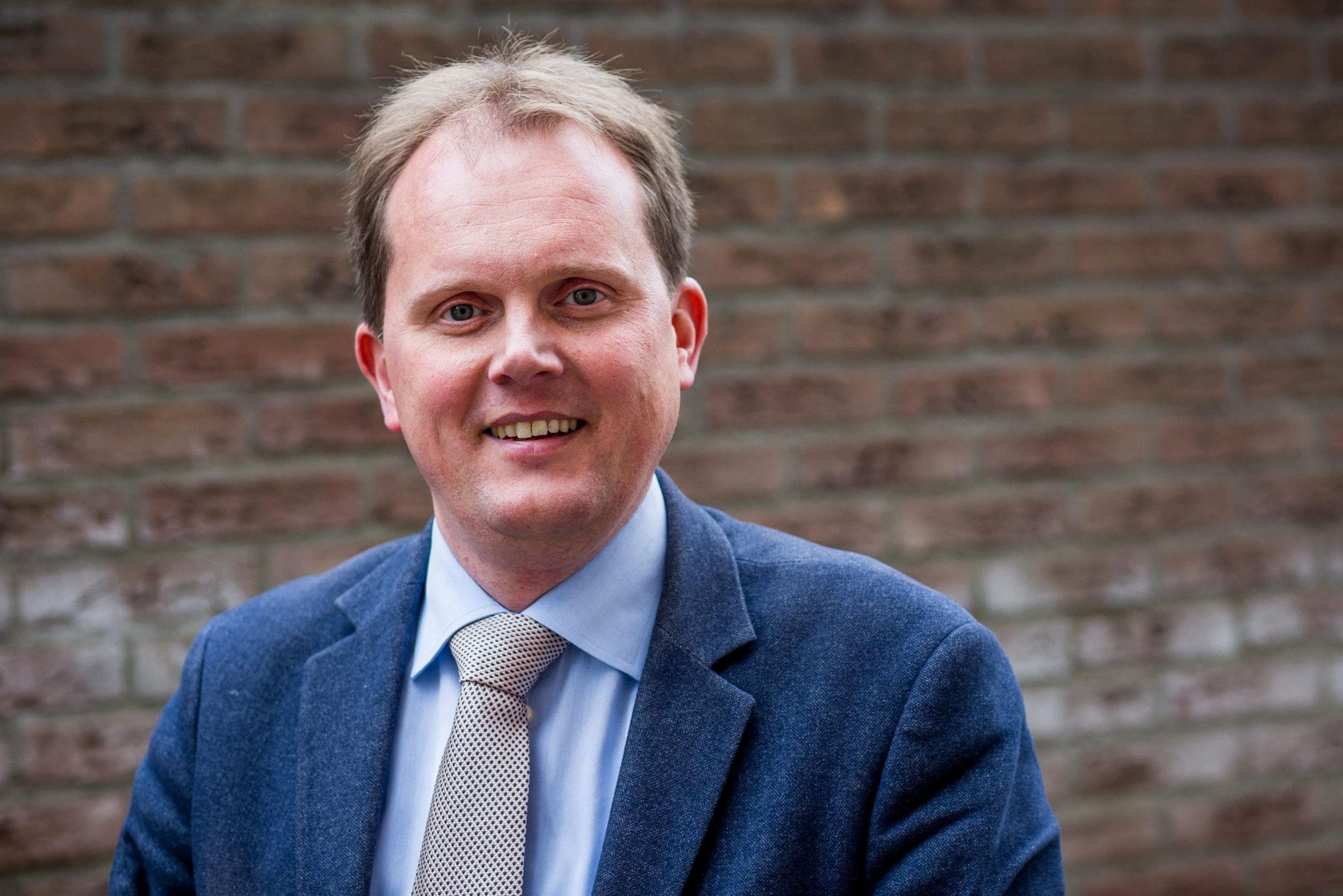 Doctor Den Hertog, een man met blond haar en blauw colbert.