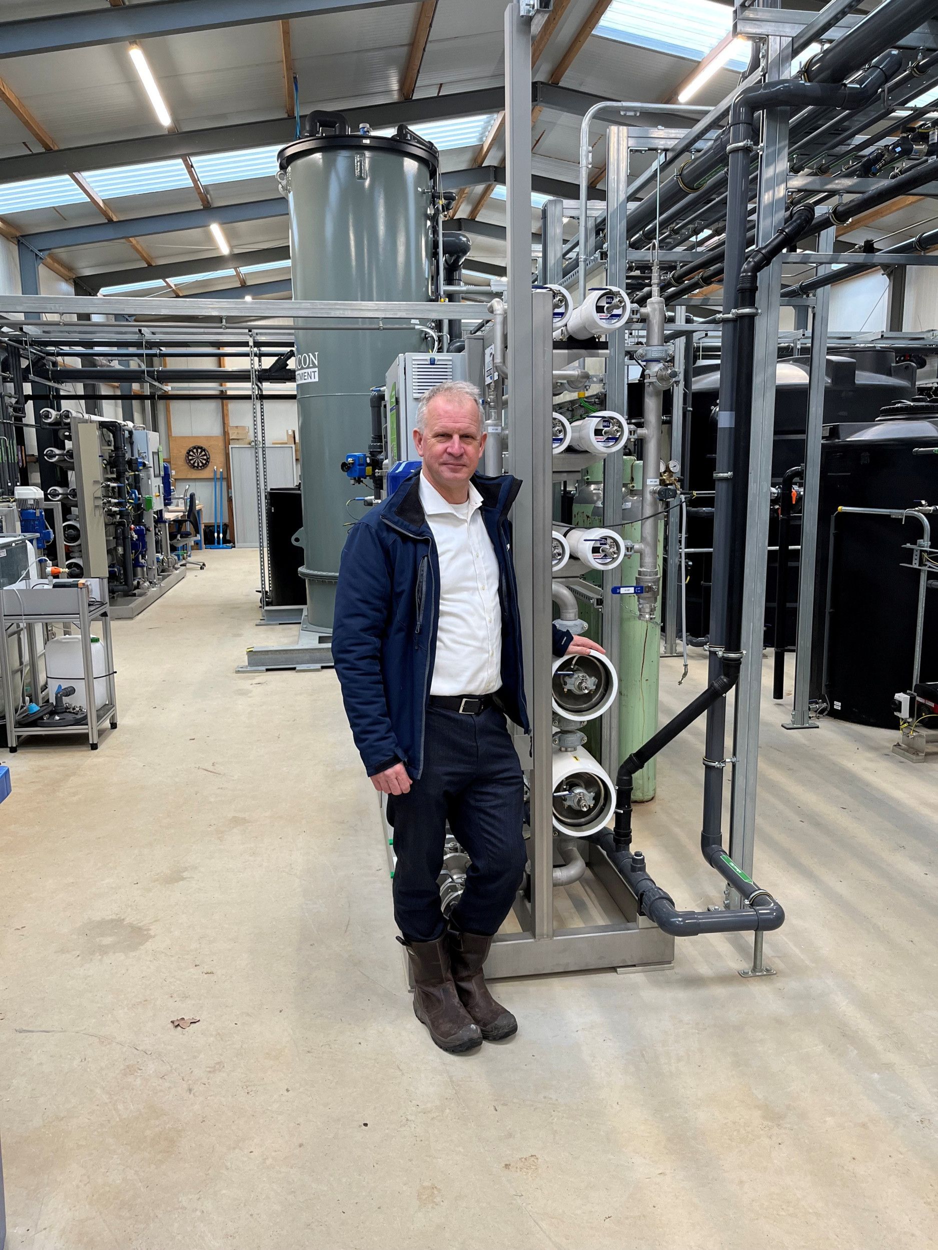 Een man staat voor een technische installatie van buizen, vaten en kokers.