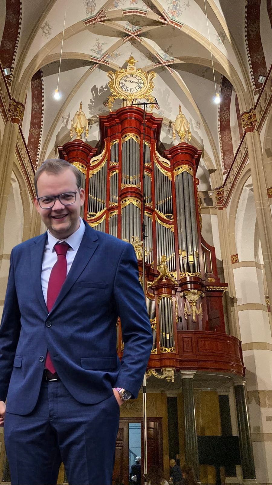 Een man in een blauw pak met rode stropdas en een bril.