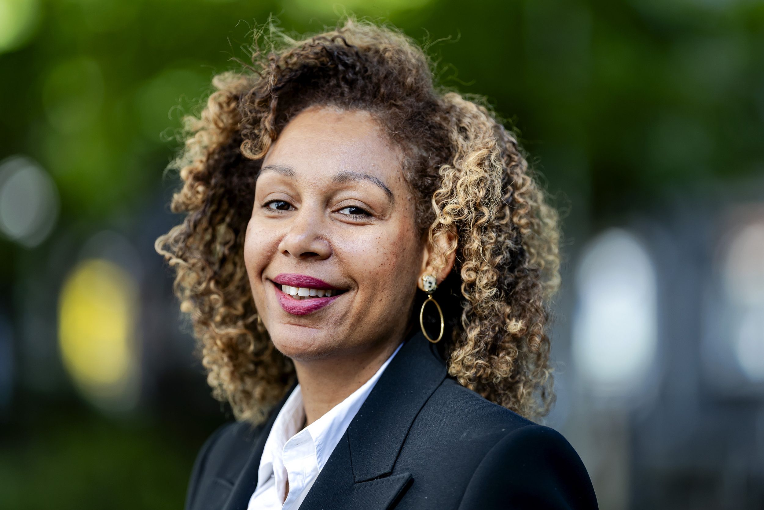 Lichtgetinte lachende dame moet halflang kroeshaar en grote ronde oorbellen.