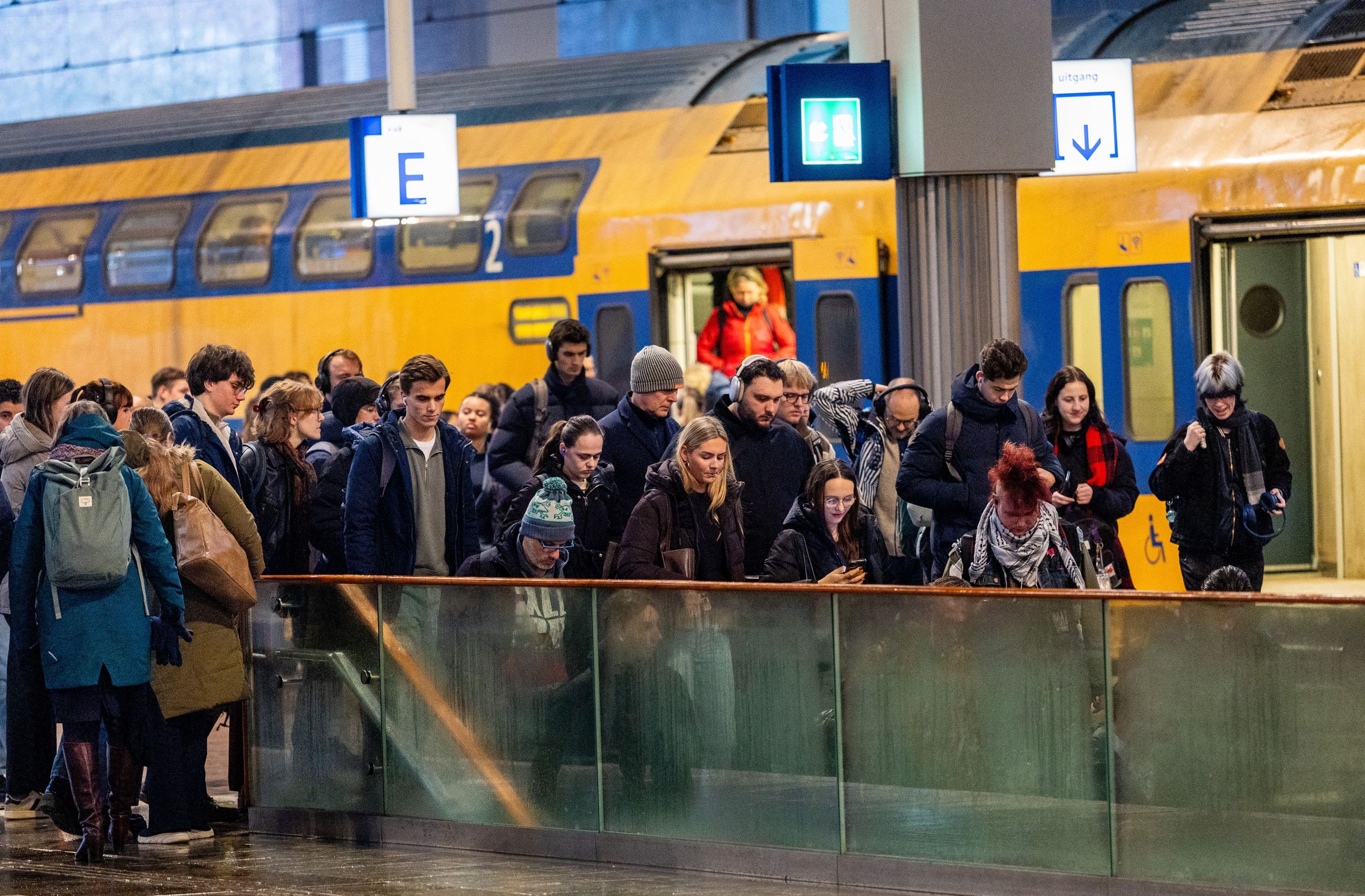 Treinreizigers hopen samen voor een trap om het perron te verlaten. Op de achtergrond stappen nog wat laatste mensen uit de trein.