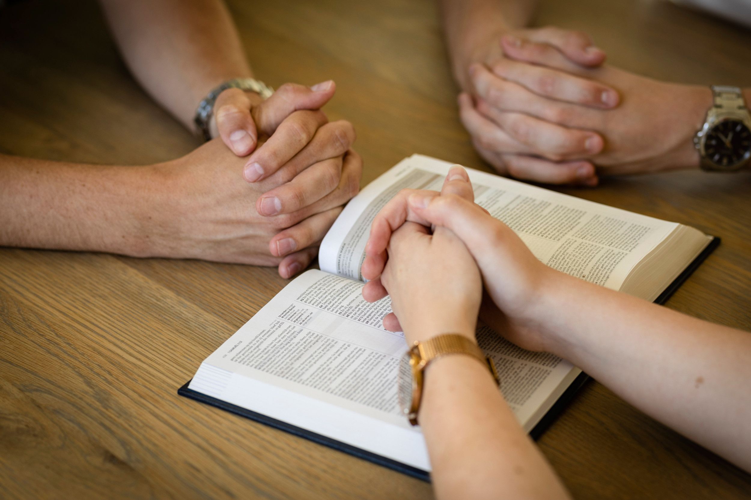 Drie paar gevouwen handen bij een open Bijbel