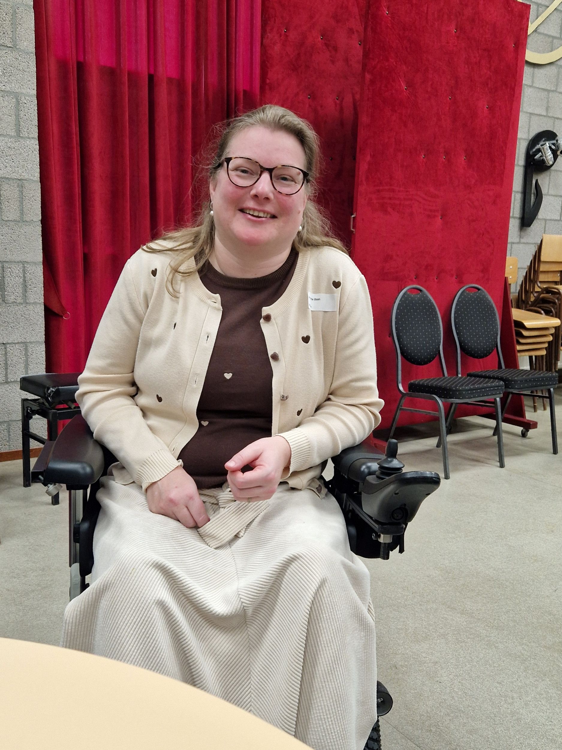 Foto van vrouw in een licht vestje en een lichte rok in een rolstoel.