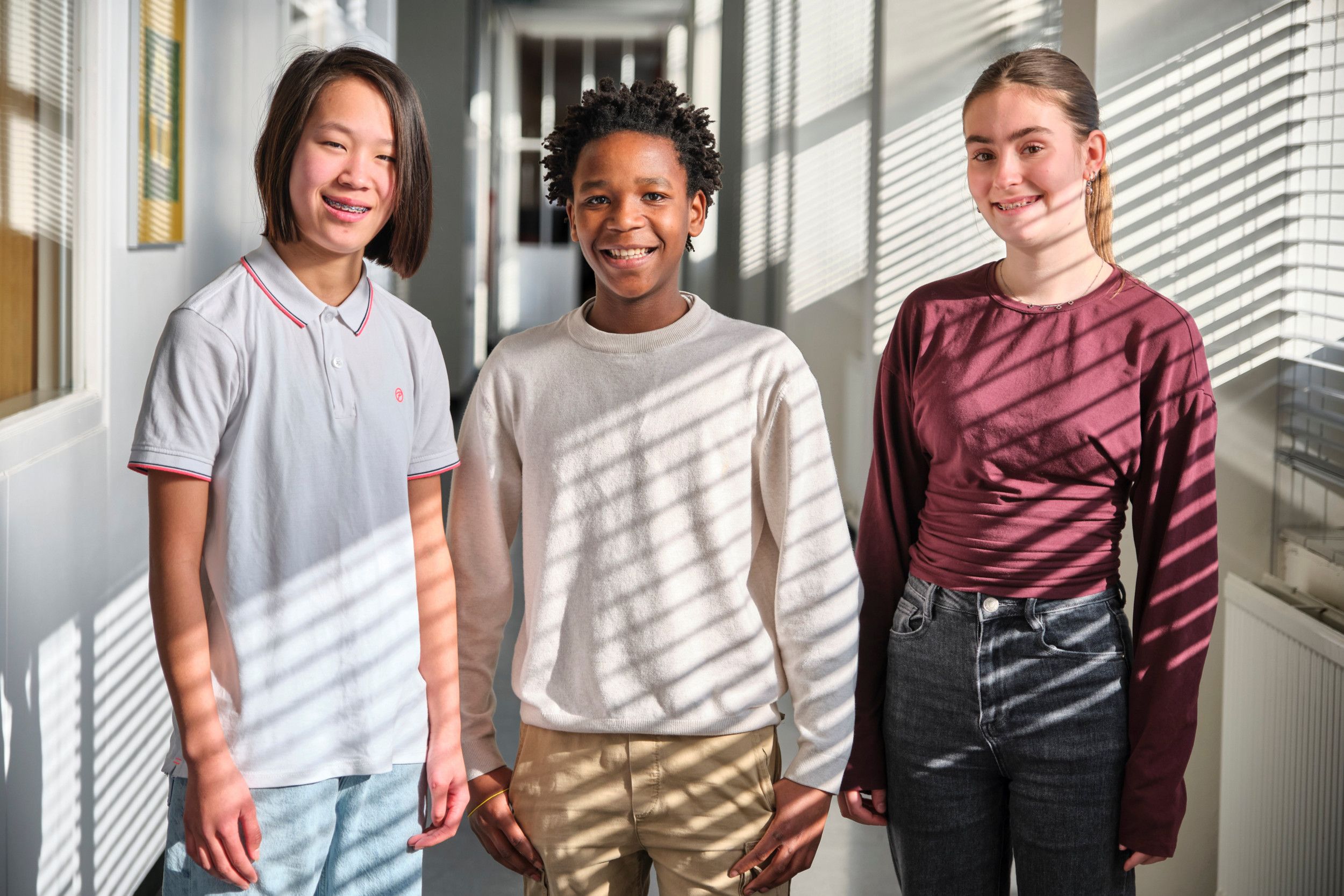 Drie leerlingen staan in de hal van een school. Ze kijken met een glimlach naar de camera.