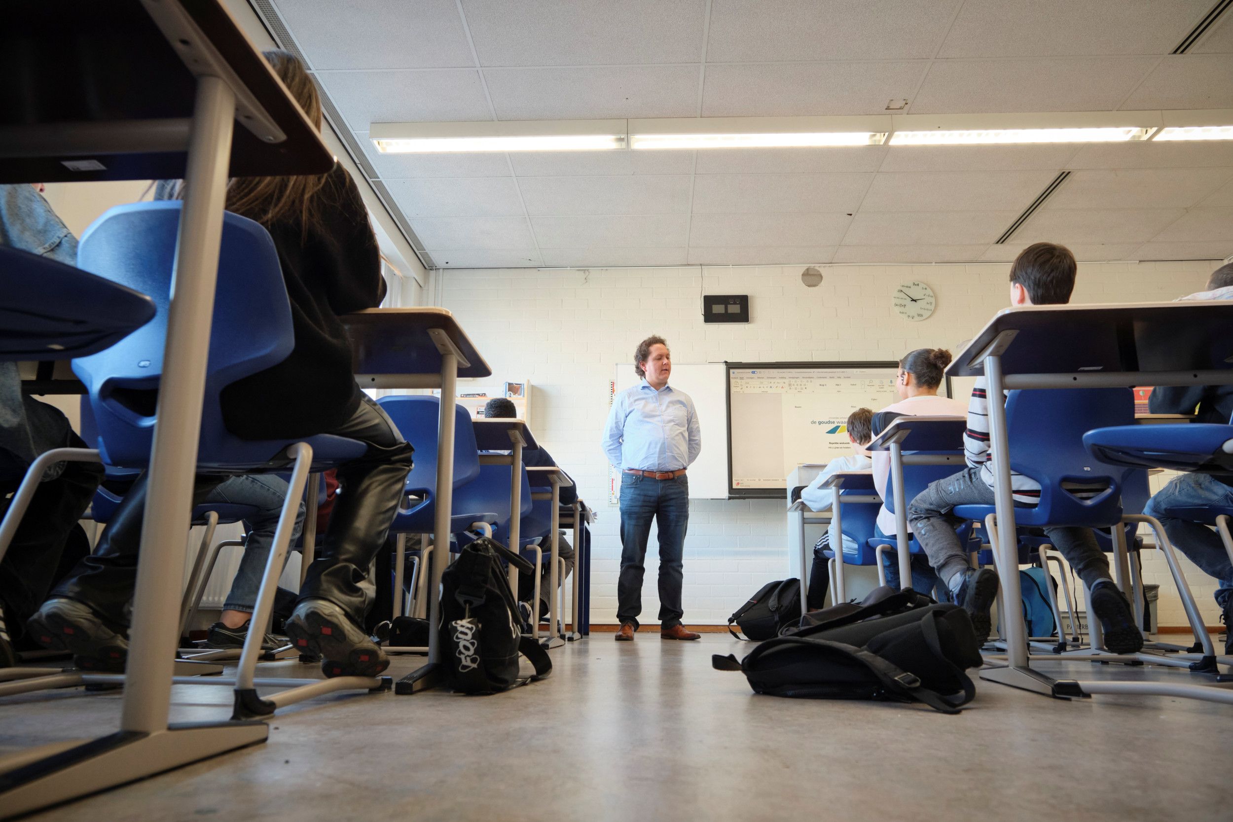 Een docent staat in zijn lokaal naast het bord.