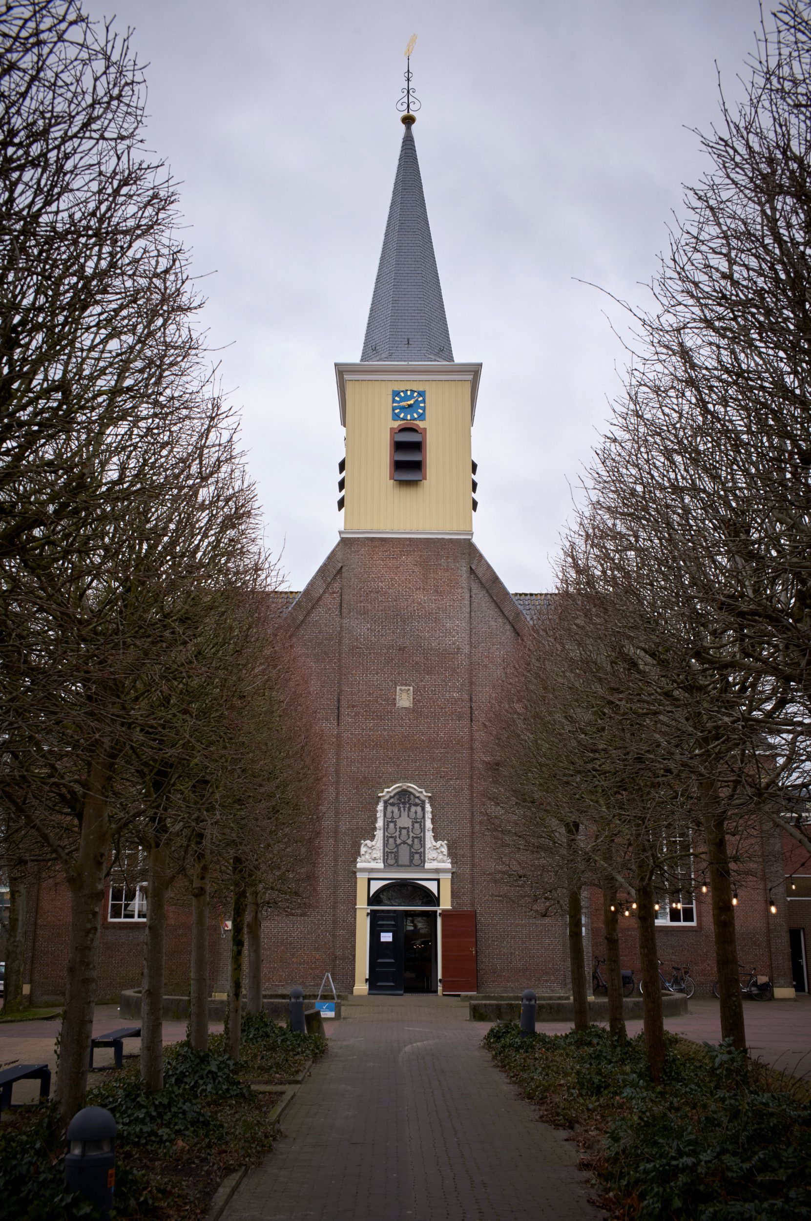 Een oude kerk, met een hoge toren. De bomen op het plein ervoor zijn kaal.