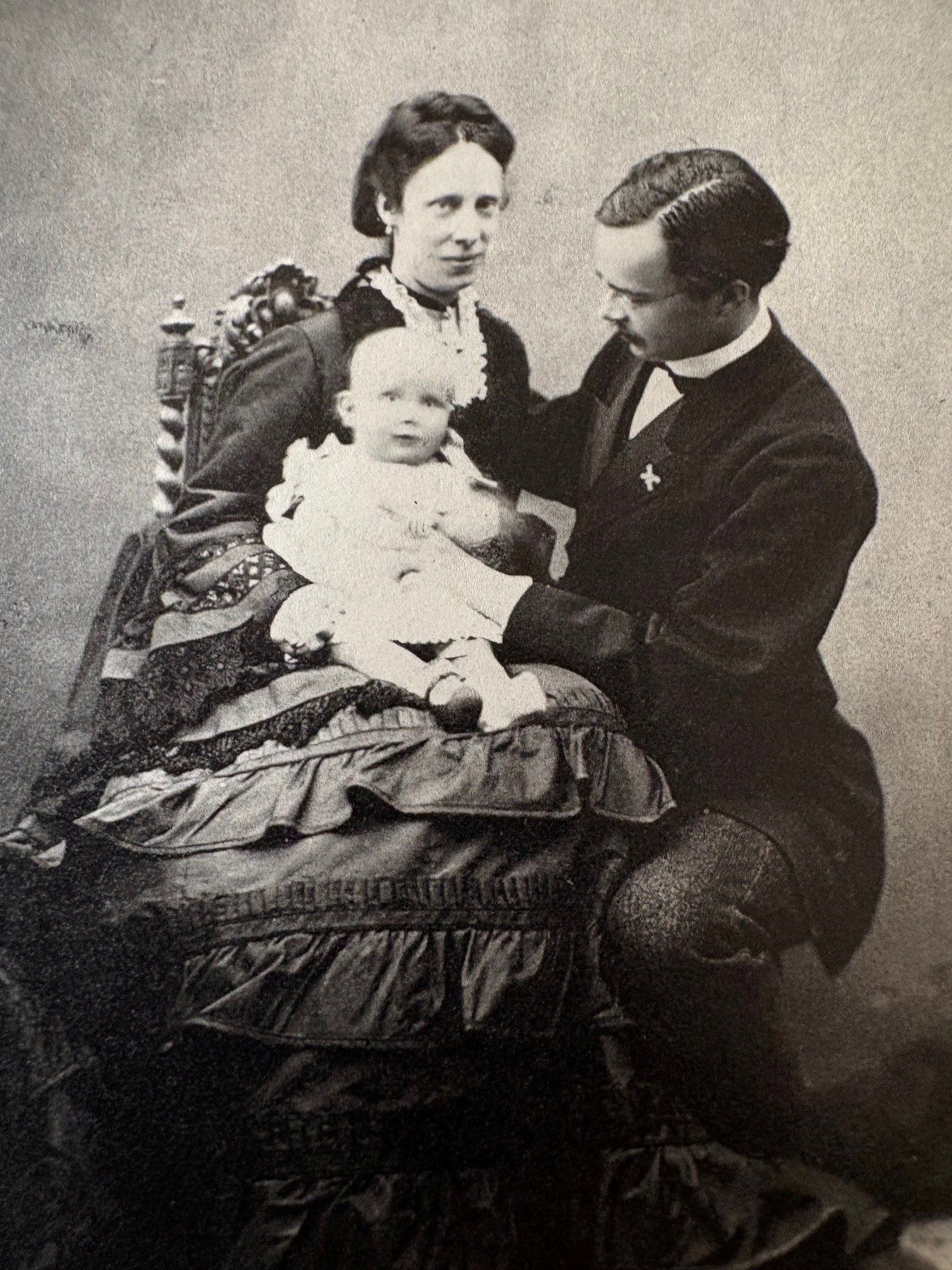 Een zwart-witfoto van een glimlachende moeder, met haar man, die naar hun jonge kind kijkt.