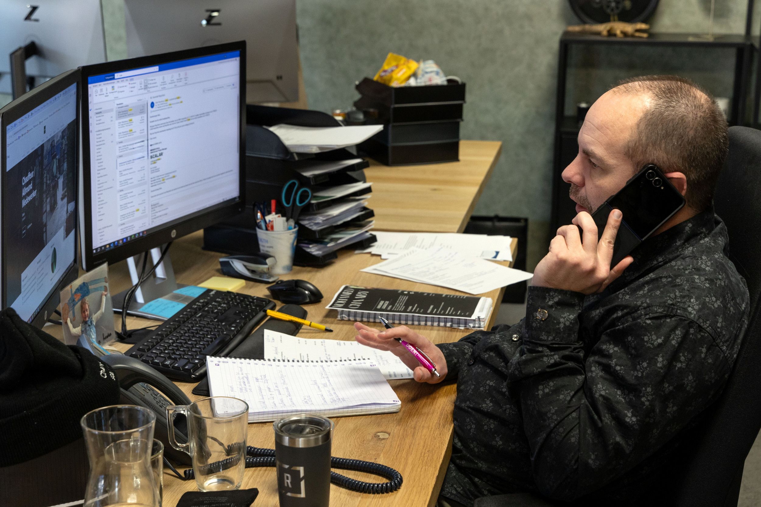 Kalende man zit aan een bureau en staart naar een scherm. Voor hem liggen schrijfblokken.