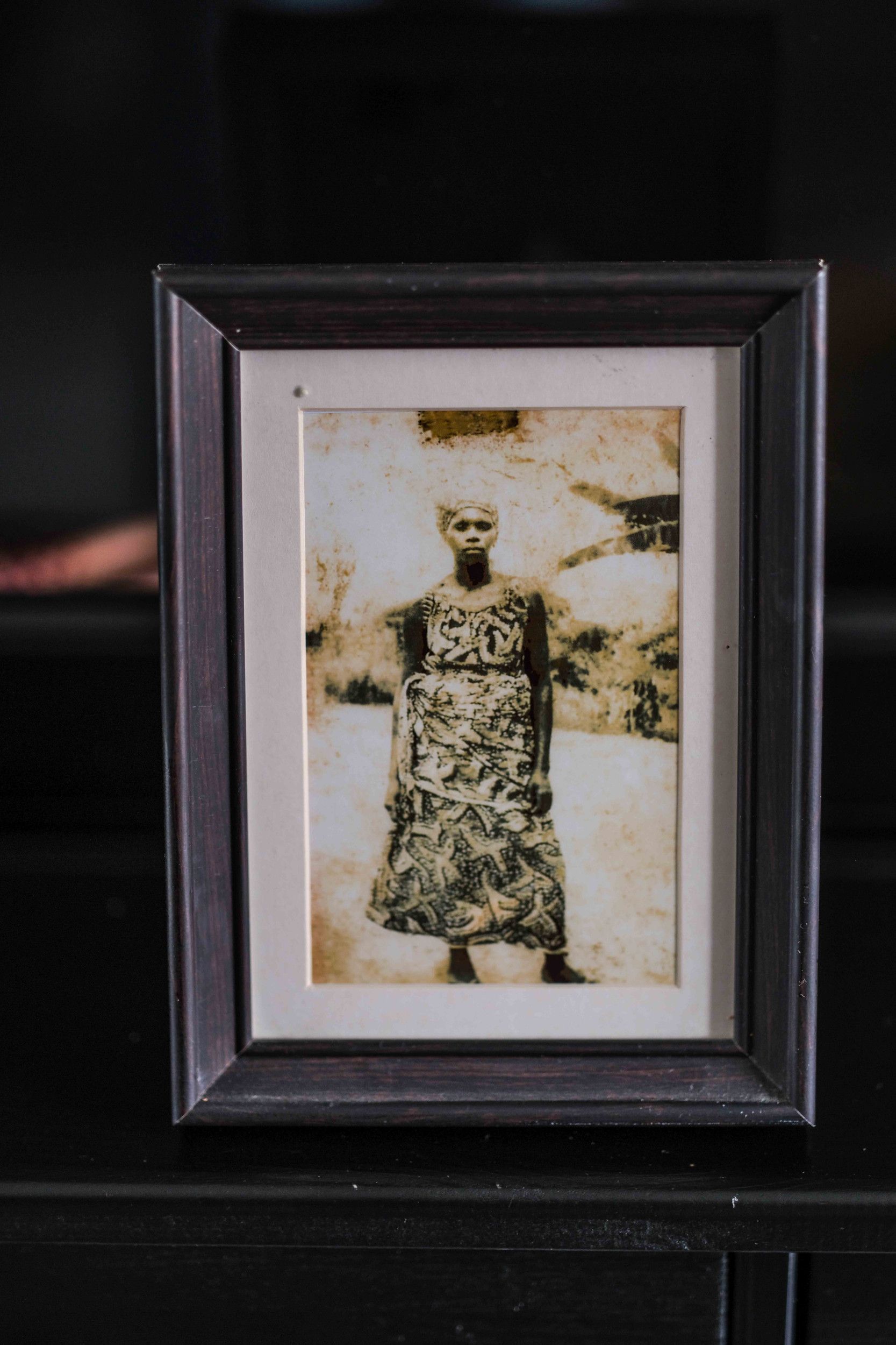 Foto in een zwart lijstje van een Afrikaanse vrouw met een hoofddoek en jurk met hetzelfde motief.