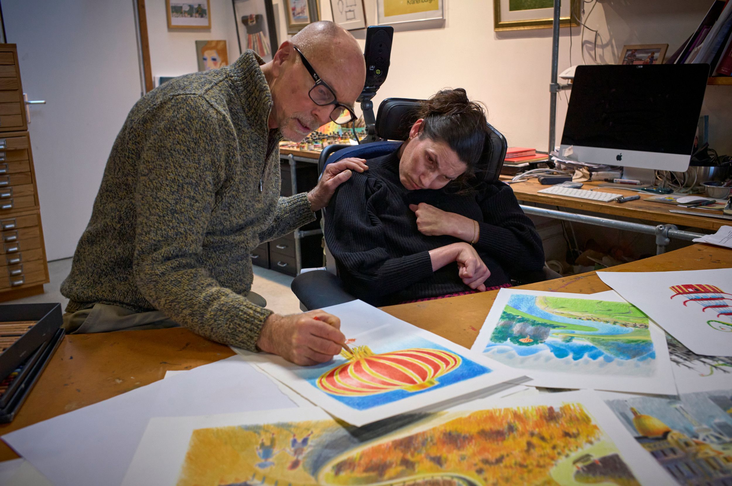 Een man met een potlood in zijn hand wijst iets aan op een tekening van een grote Chinese ballon. Zijn linkerhand ligt op de schouder van de vrouw naast hem.