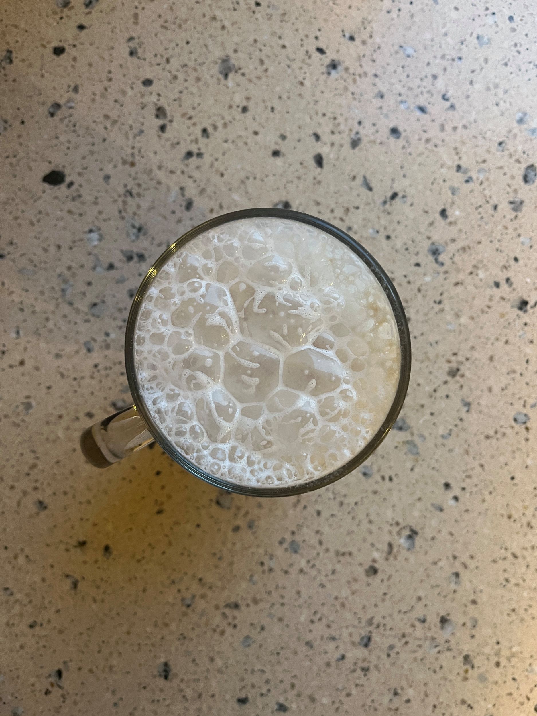 Bovenaanzicht van een glas met daarin opgeklopte melk met heel grote bellen