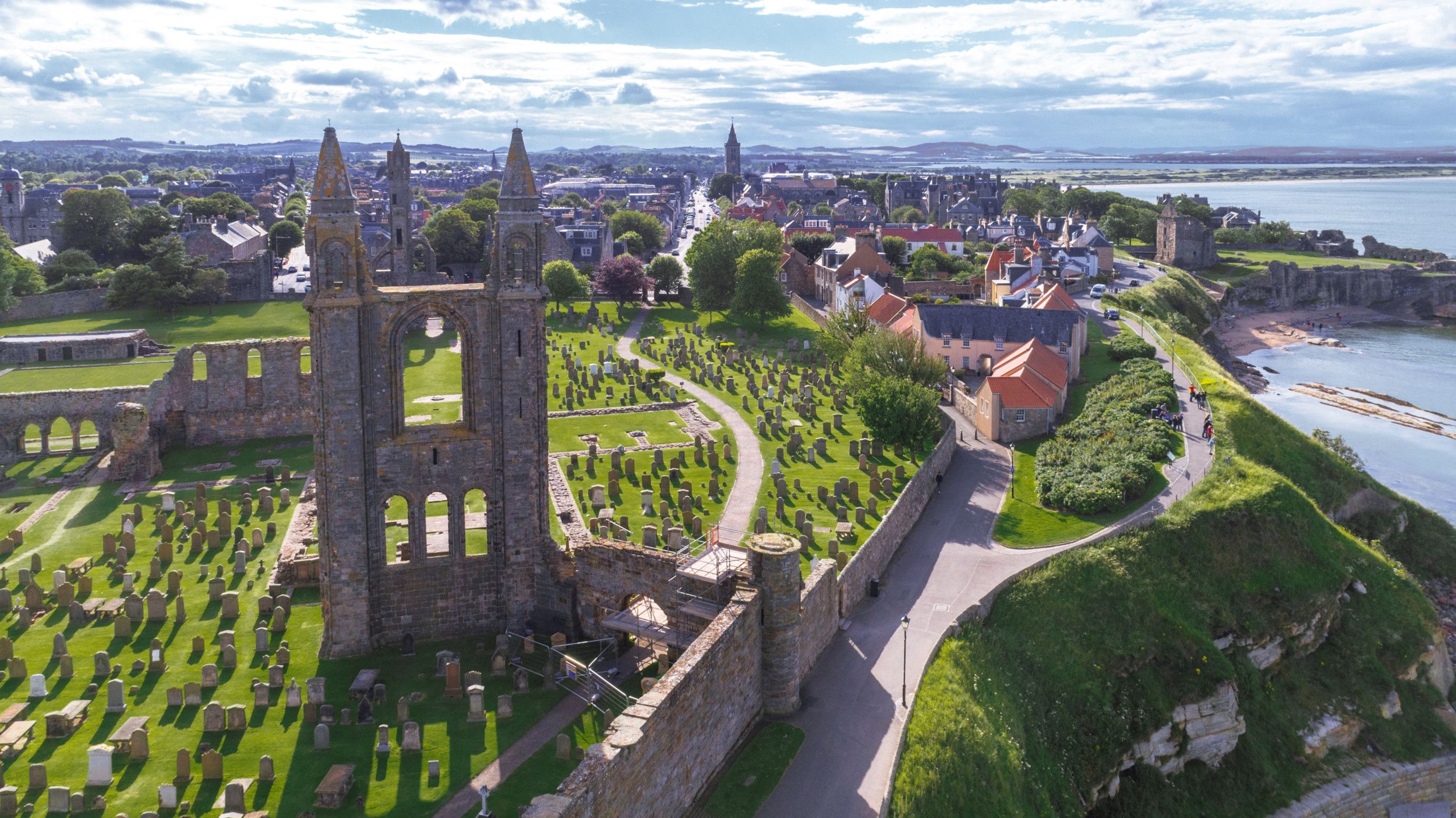 Op de voorgrond de ruïne van een oude kerk met grafstenen. Op de achtergrond een stad aan de zee.